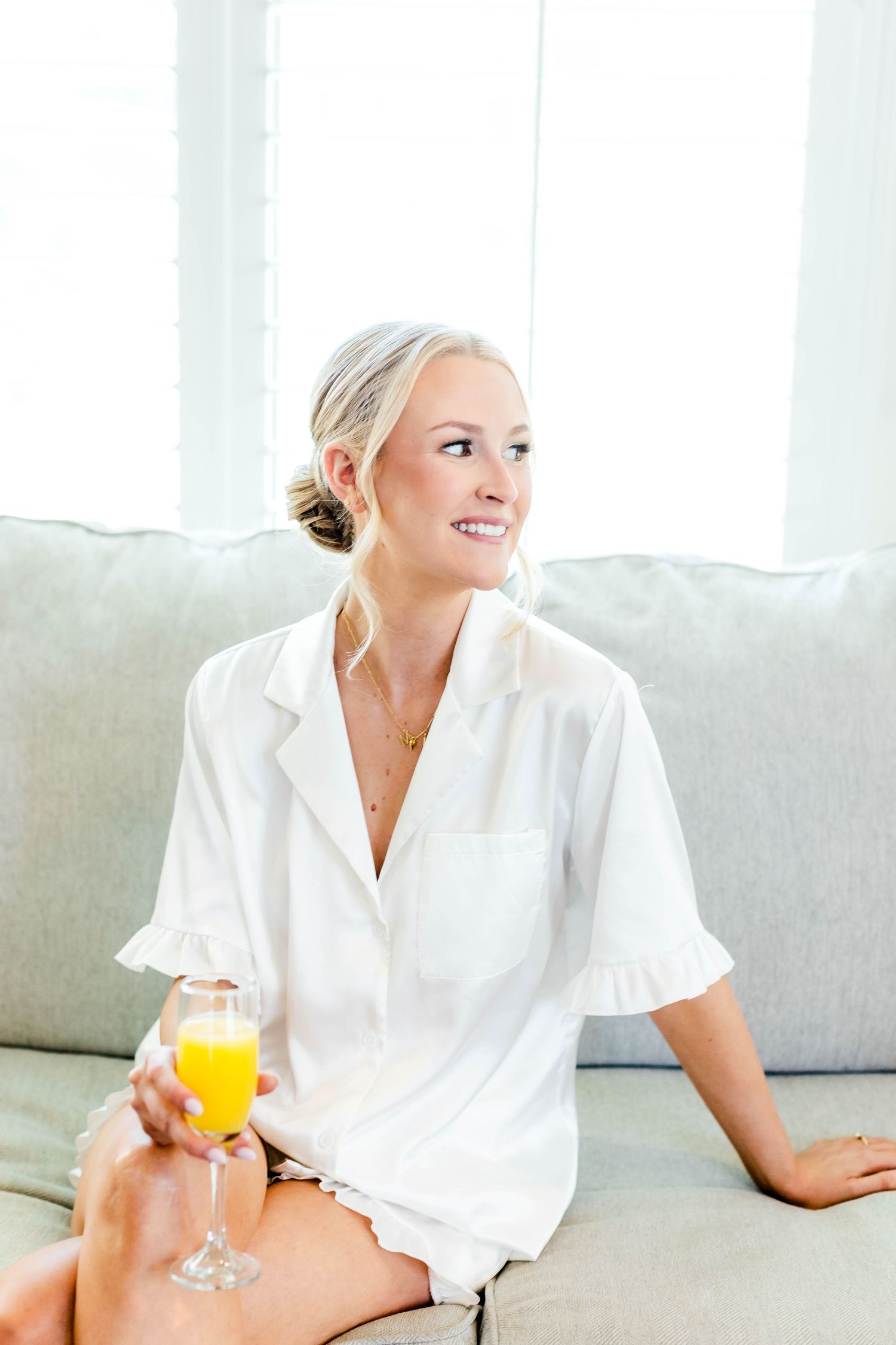 Person in white robe relaxing on grey couch with orange juice.