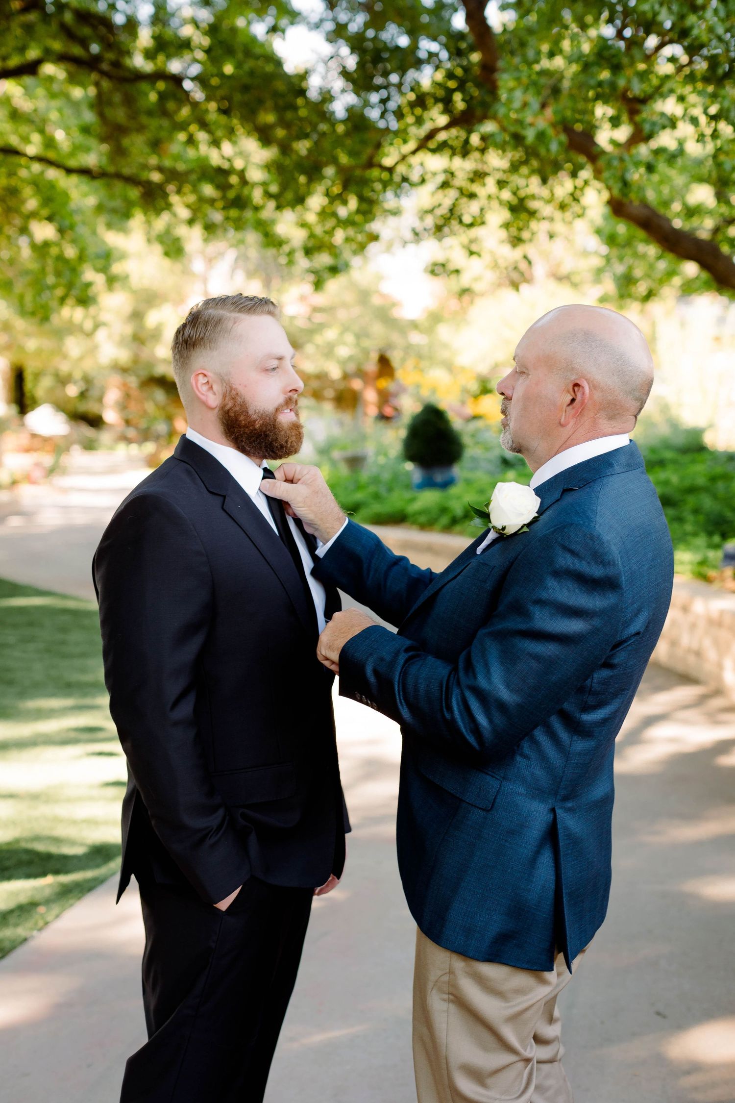 Two people in formal attire share an emotional moment during a wedding ceremony outdoors.
