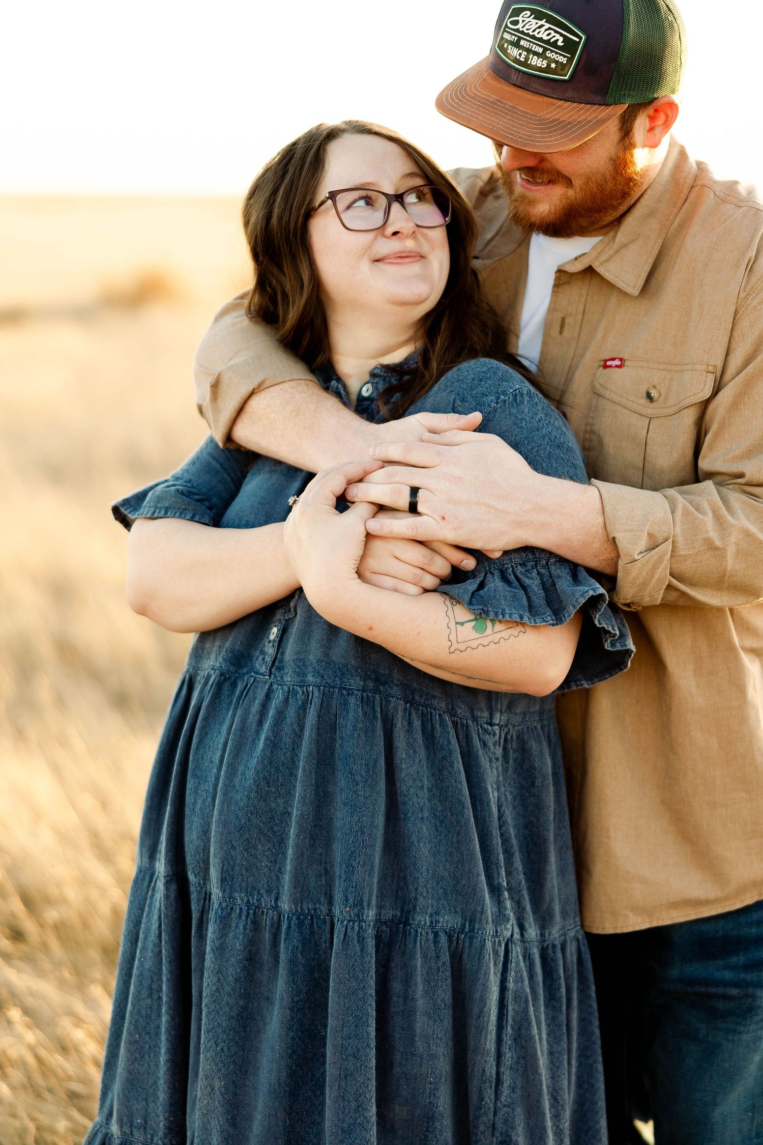 A tender family moment captured in a field at golden hour with warm sunlight illuminating the scene.