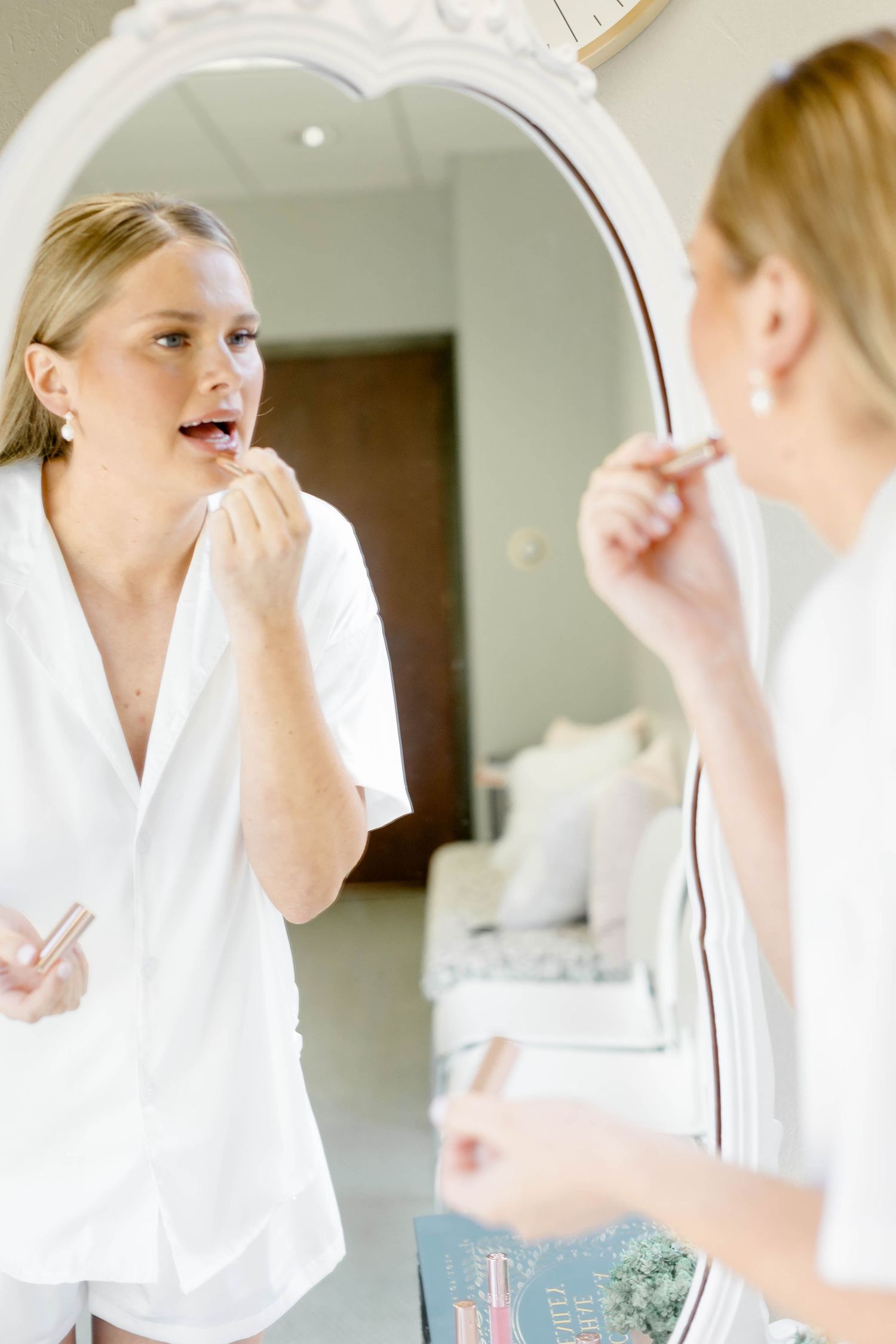 Bride getting ready in front of mirror on wedding morning wearing white robe.