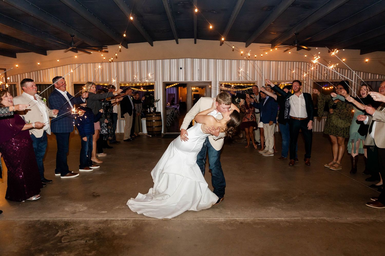 Wedding guests watch as the newlyweds perform their first dance in a dimly lit reception venue.