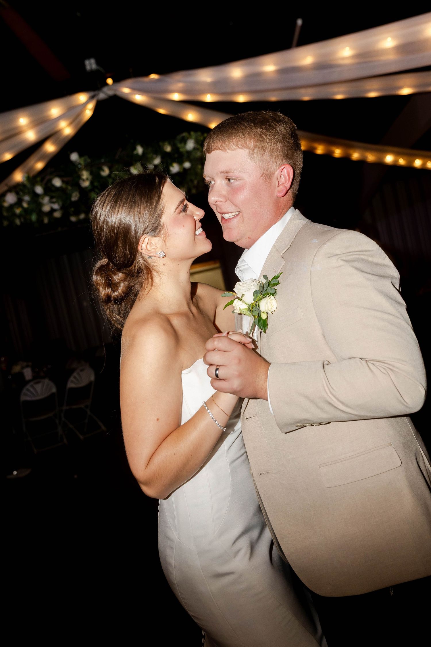 Couple dancing under string lights at an evening wedding reception.