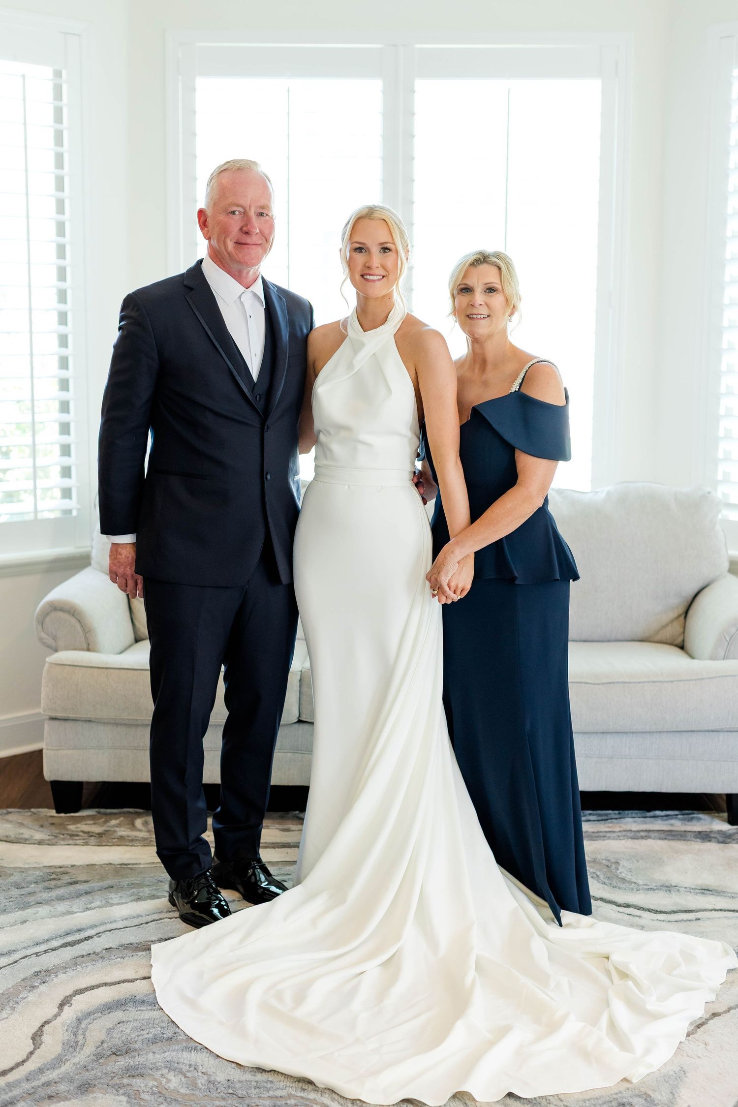 Wedding party poses together in elegant white and navy formal attire against a bright interior.