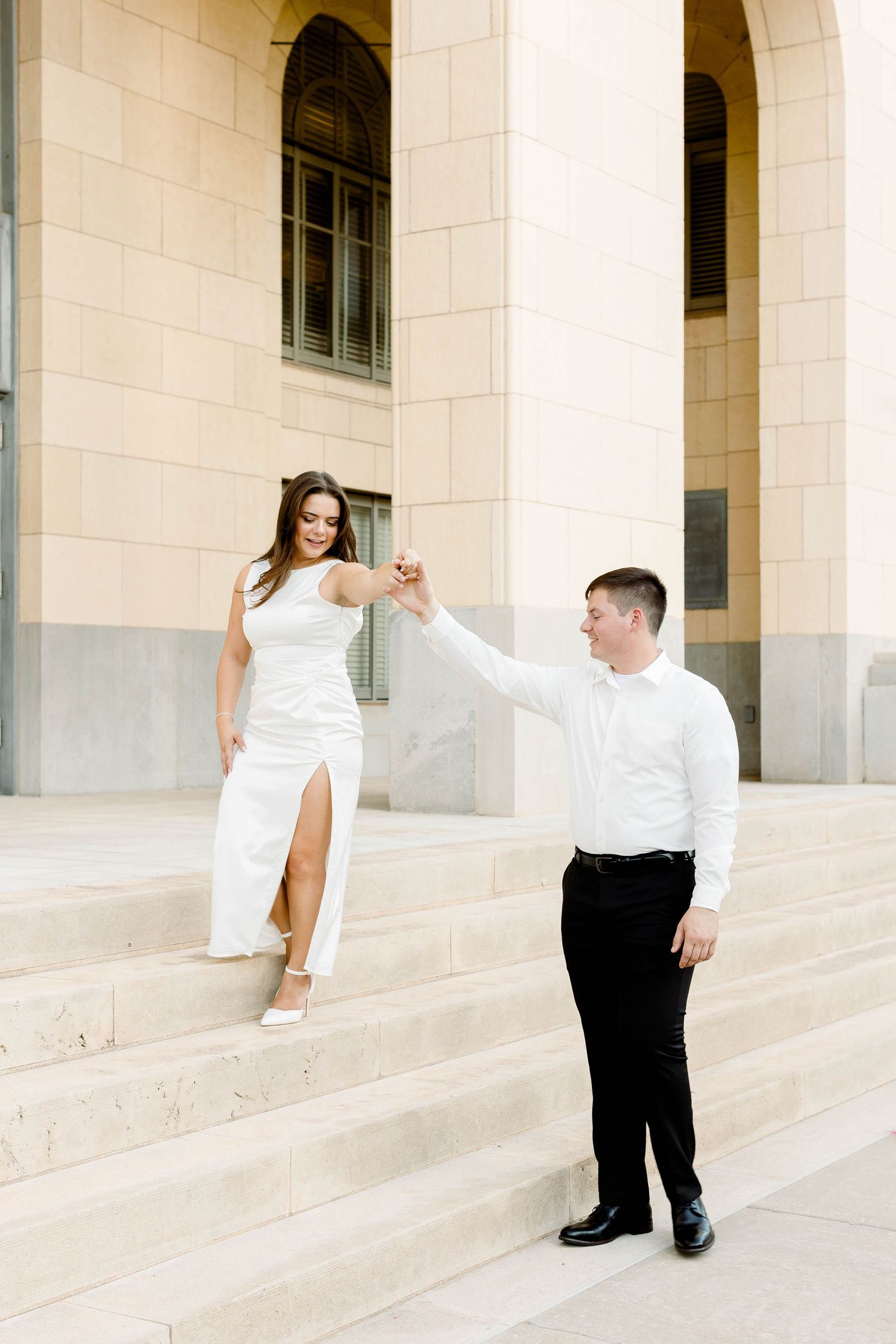 Couple poses playfully on wide stone steps with elegant archways in the background.