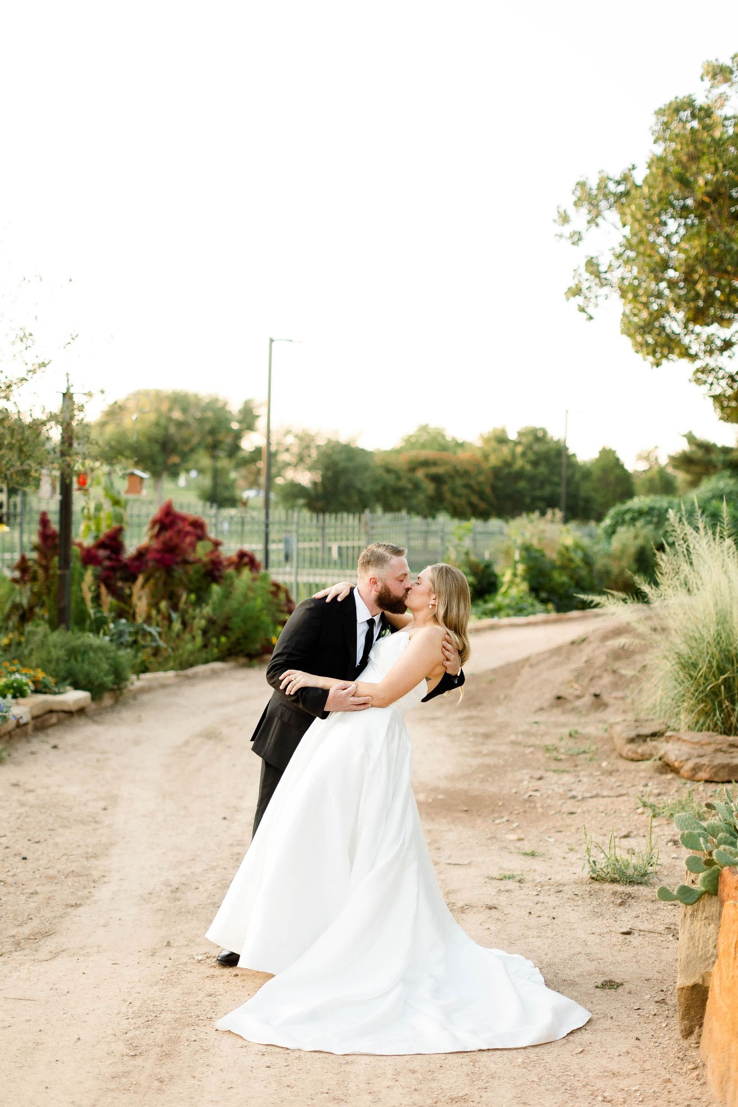 A romantic wedding couple shares intimate moments in a desert garden setting at sunset.