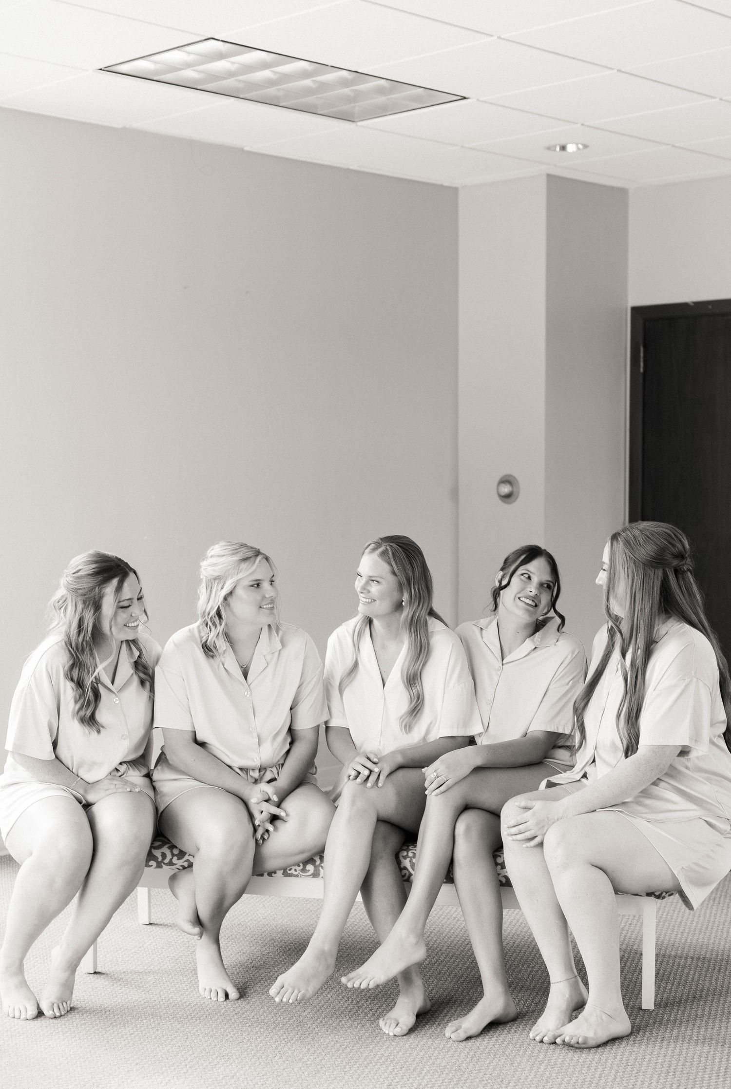 A group of people in white clothing sit in a row on the floor making playful gestures in a minimalist setting.