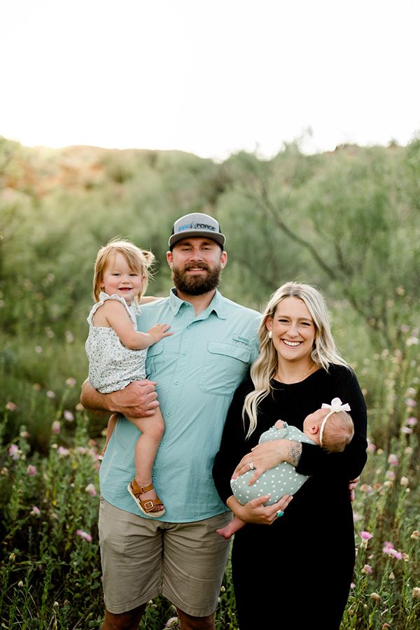 Family portrait session in a natural outdoor setting with wildflowers and warm lighting.