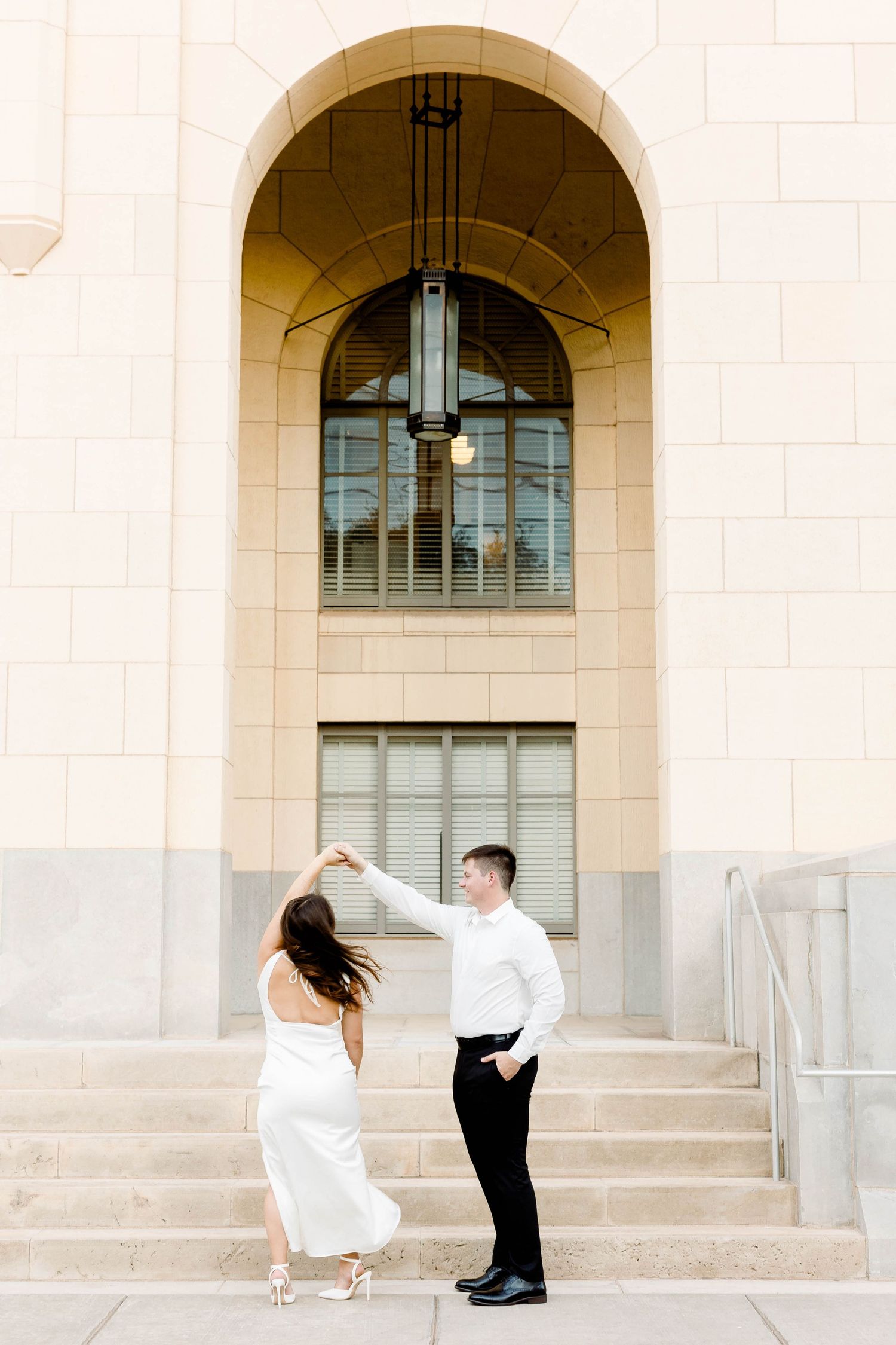 Couple shares a romantic dance moment on stone steps with arched architecture.