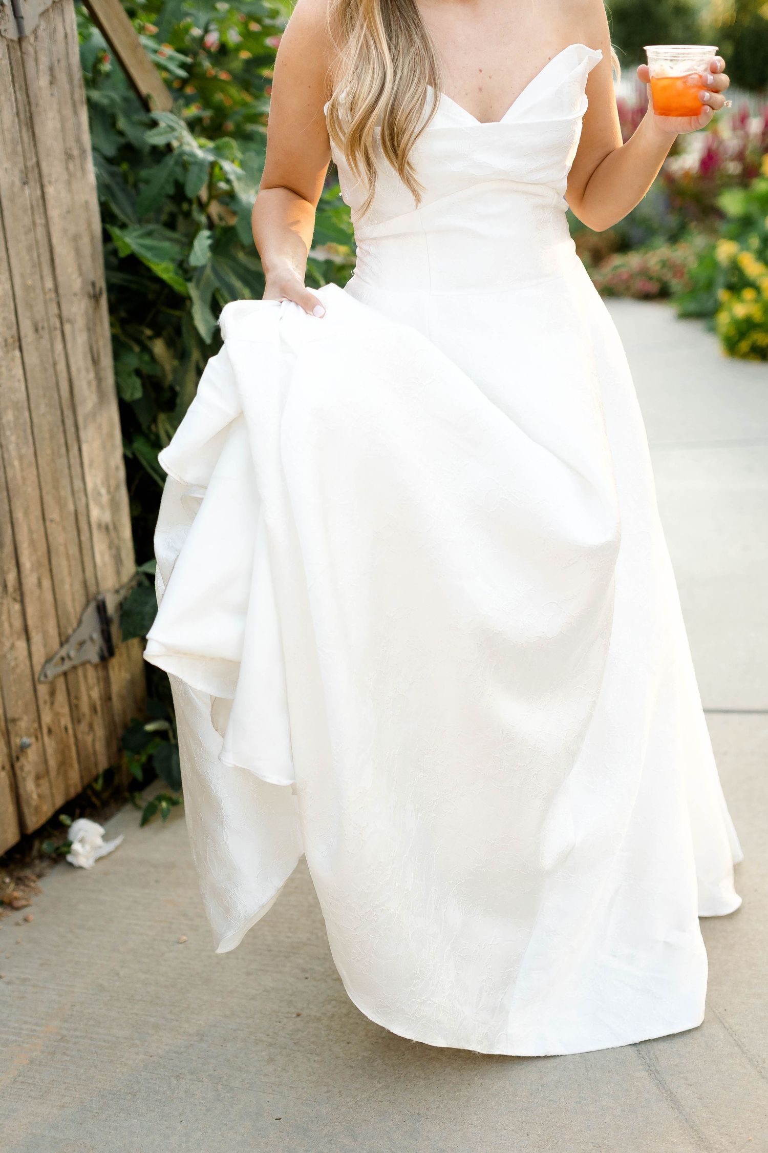 Close-up details of a flowing white wedding dress train on stone pathway.