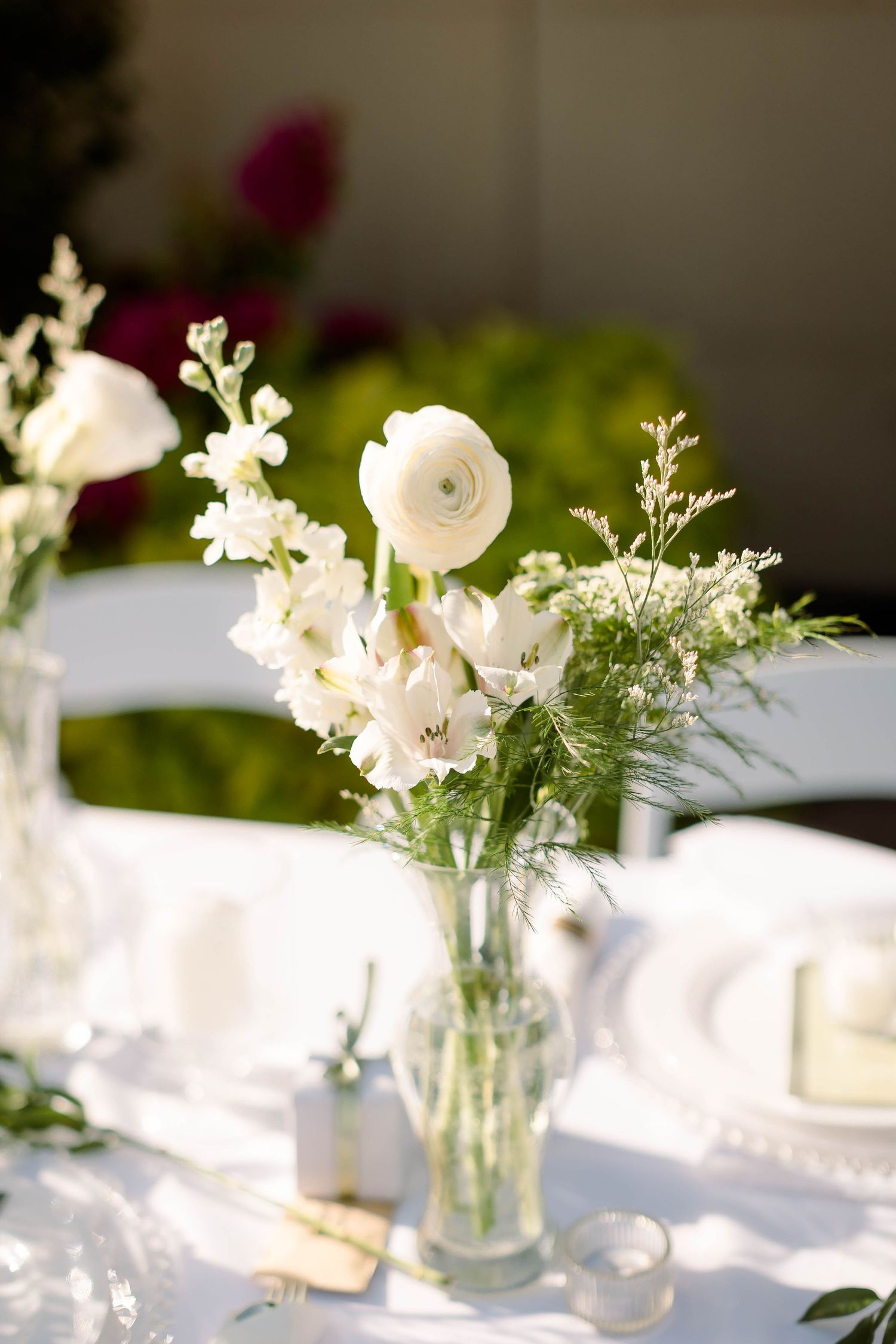 Delicate white floral centerpieces in glass vases arranged on a white tablecloth for an elegant wedding reception.