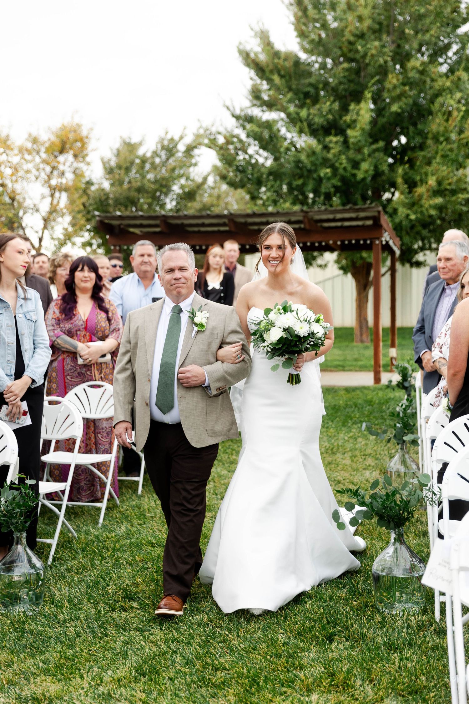 Wedding guests seated in white chairs on a lawn watching the ceremony procession.