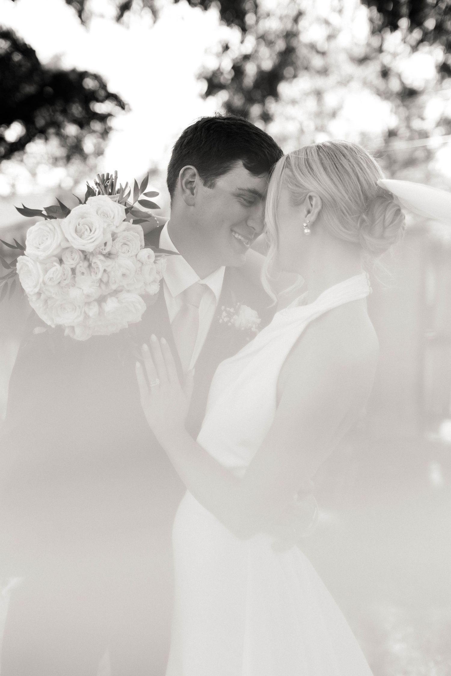 Dreamy black and white wedding photo of newlyweds sharing an intimate moment with a white bouquet.