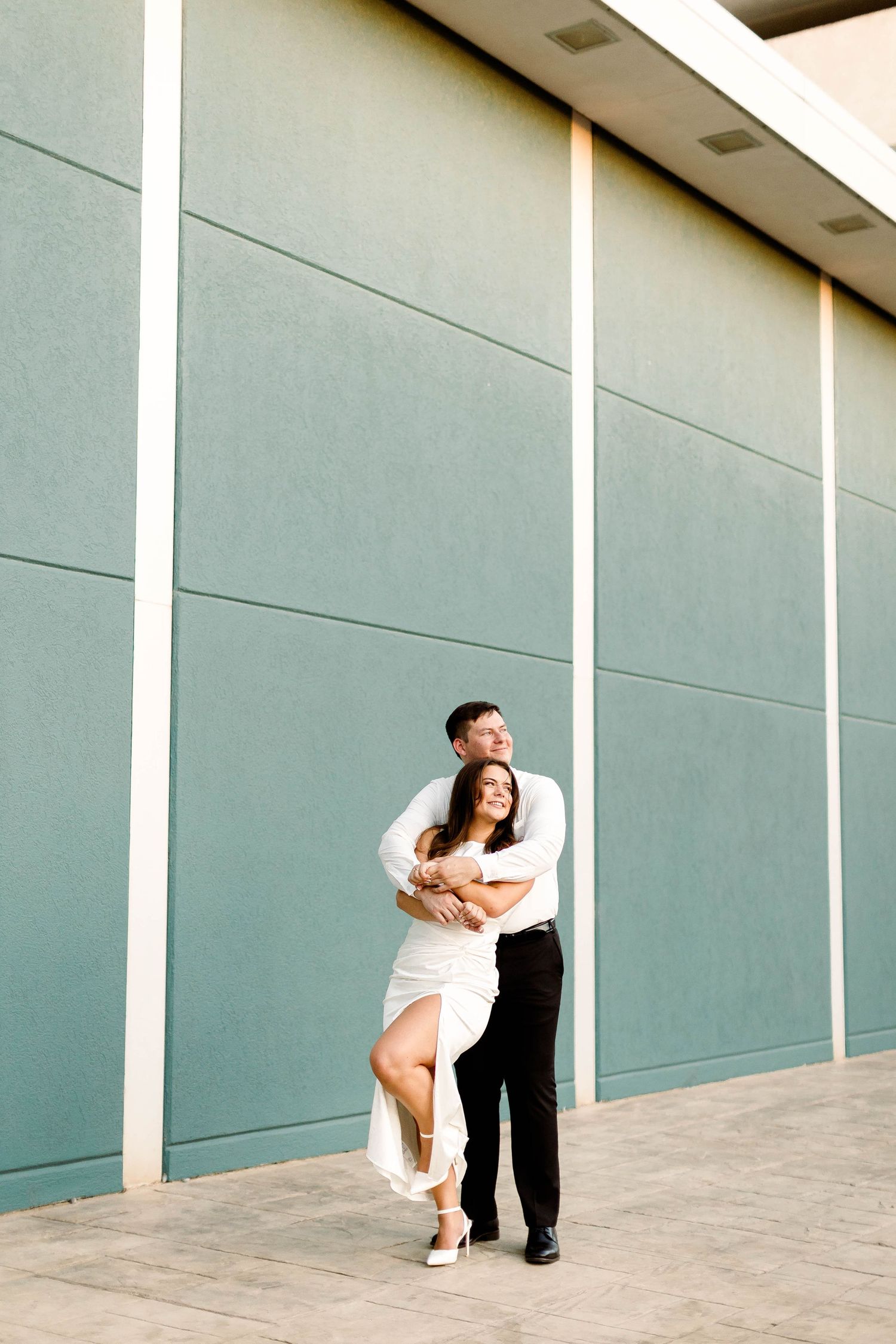 An artistic engagement photo series showing a couple posing playfully against modern architecture.