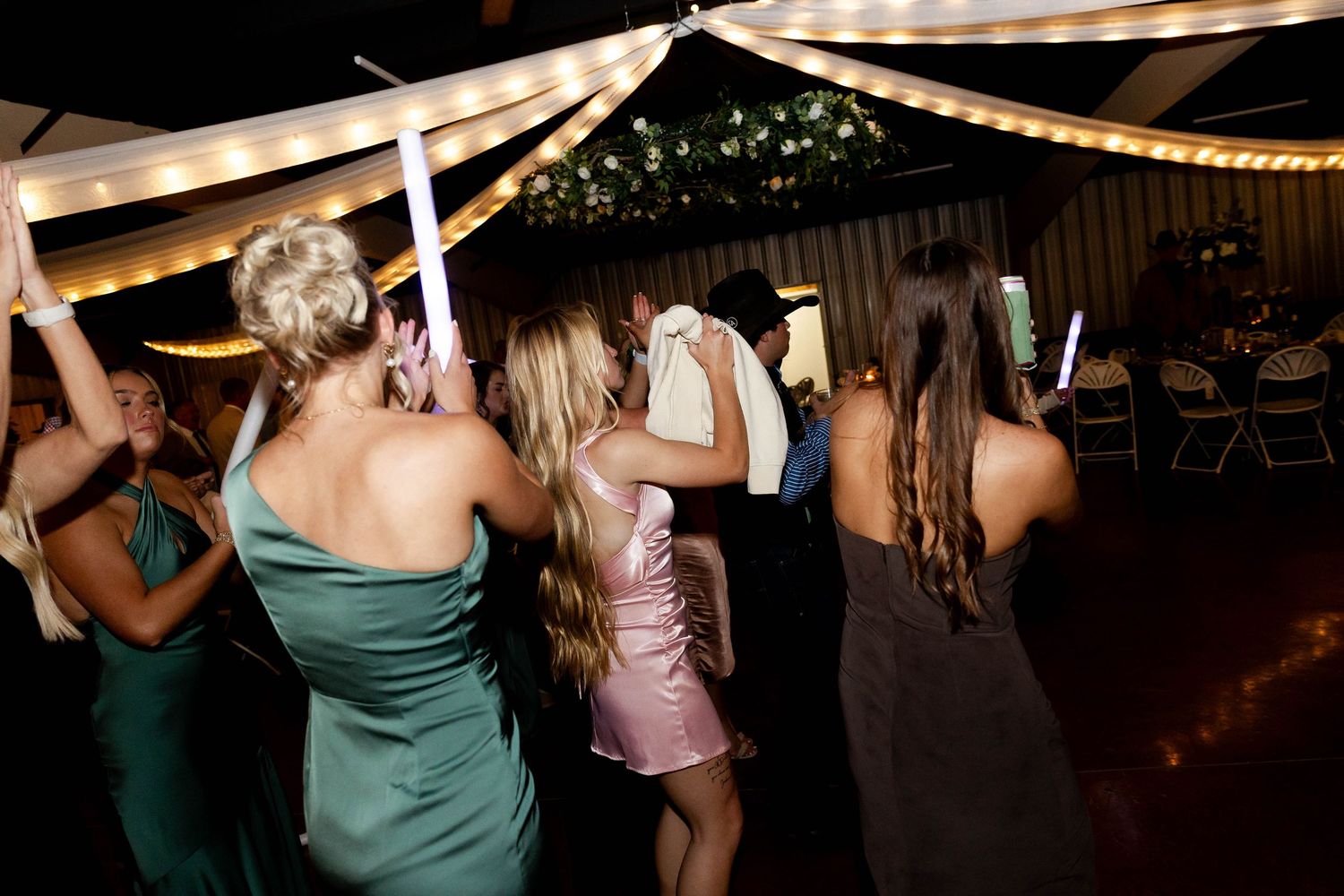 Wedding reception dance floor filled with guests under draped fabric and string lights.