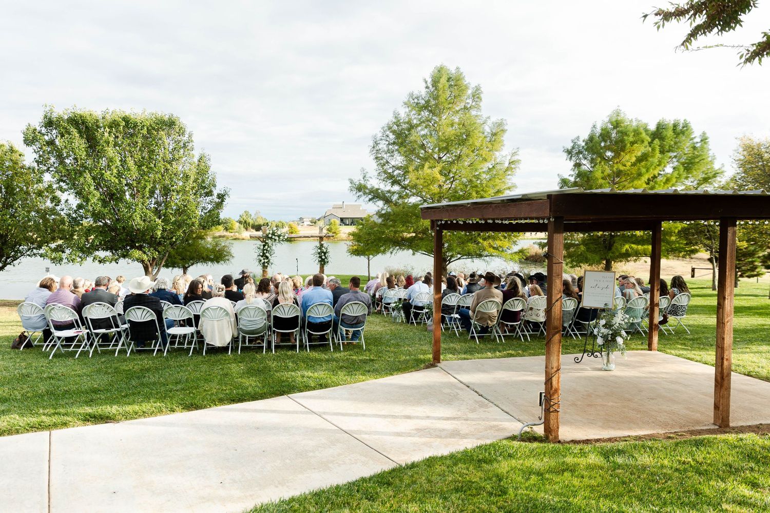 Outdoor wedding venue setup with wooden pergola and white chairs arranged on grass.