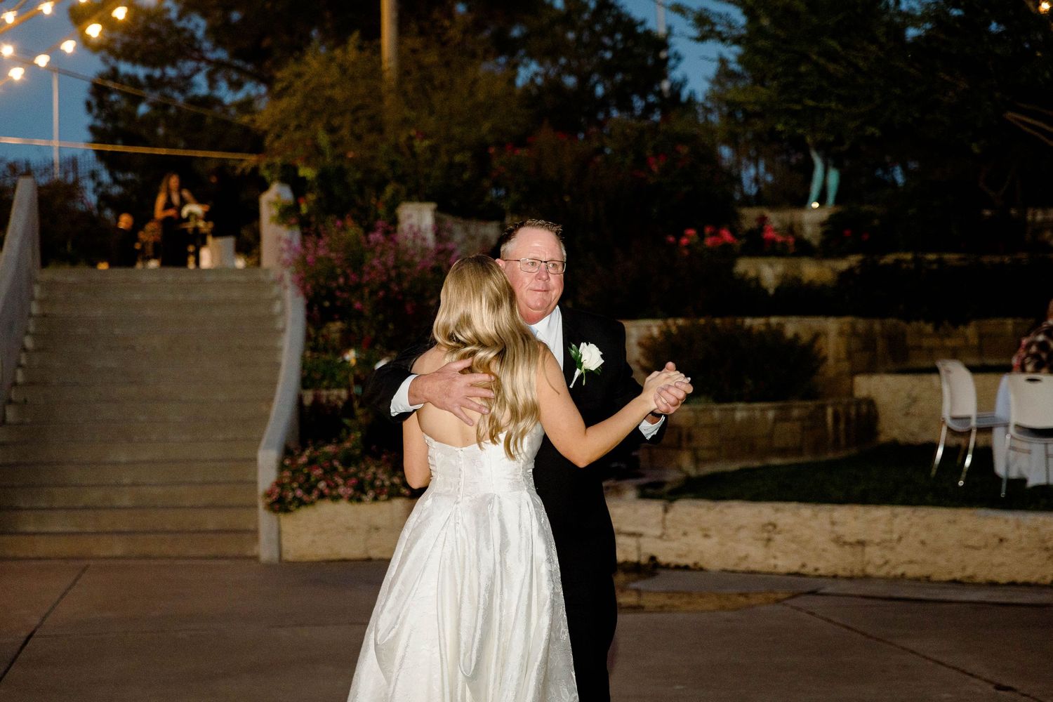 A couple dancing together at dusk under outdoor string lights at their wedding reception.