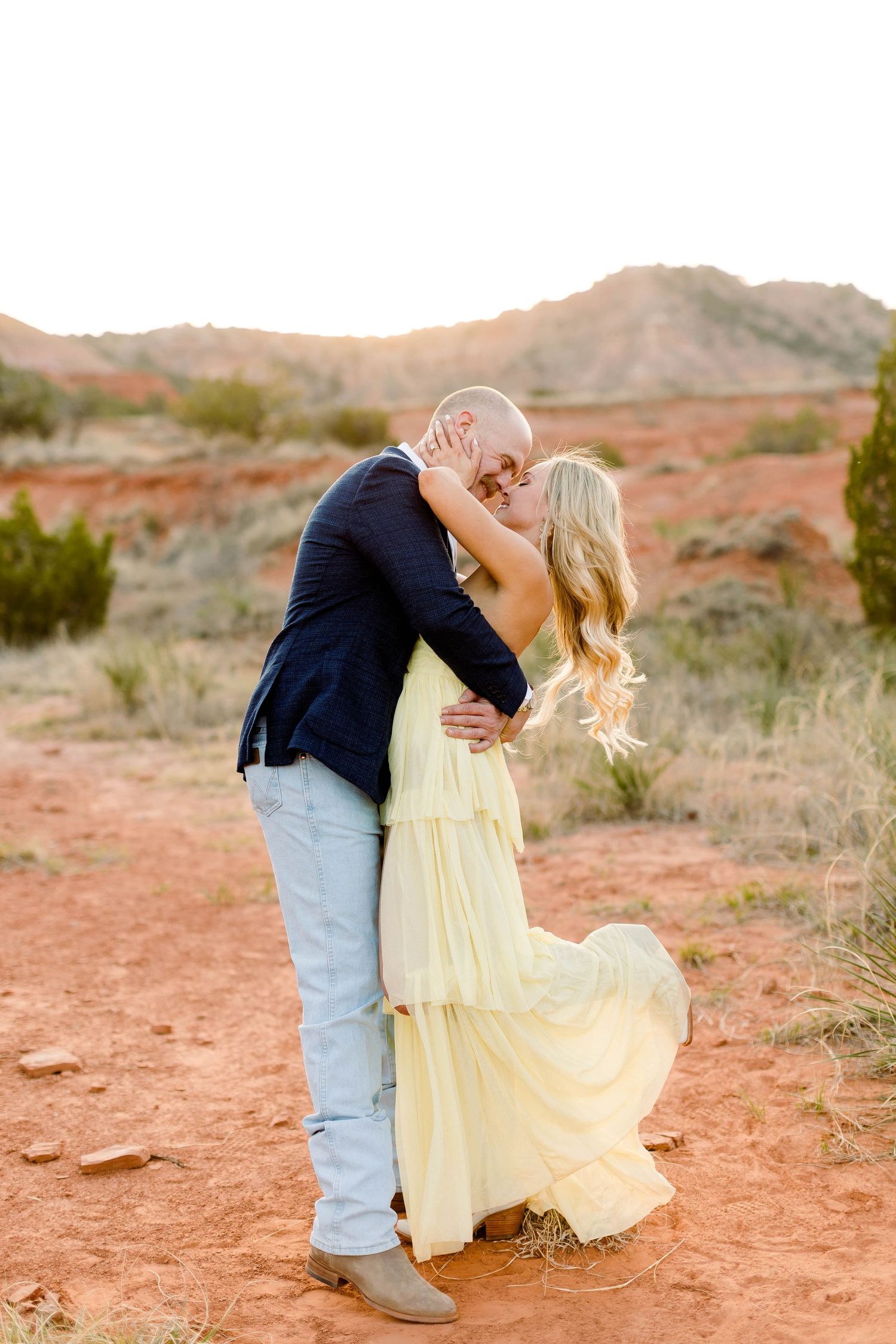 Dramatic dip pose during desert engagement shoot with mountains in background.