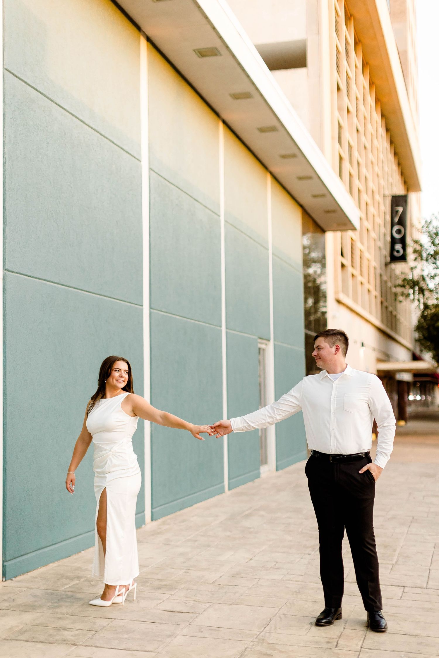 A couple in white and black formal attire poses playfully in a series of photos against a modern building exterior.
