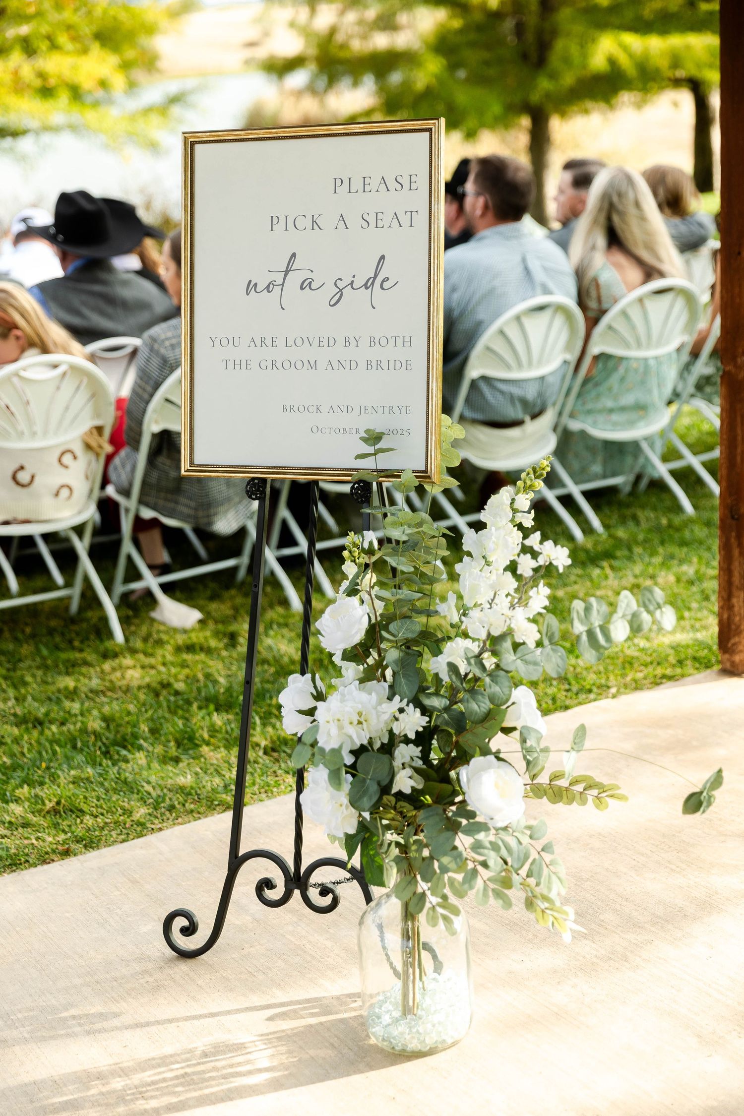 Wedding ceremony seating area with white chairs and floral decorations on display stands with elegant signage.