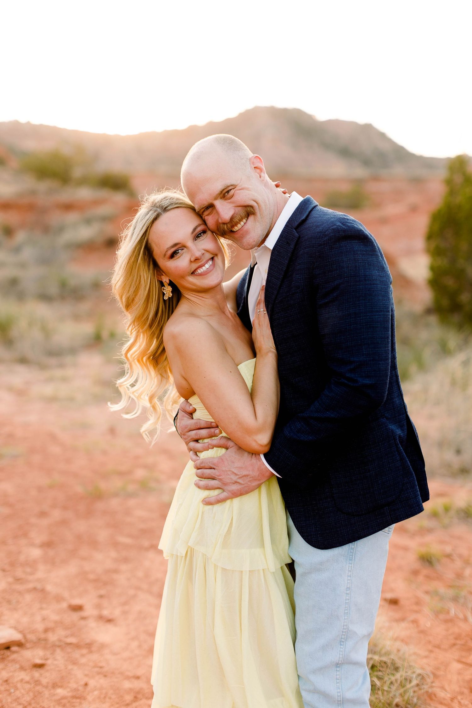 Sweet embraces captured during desert engagement photo session at sunset.