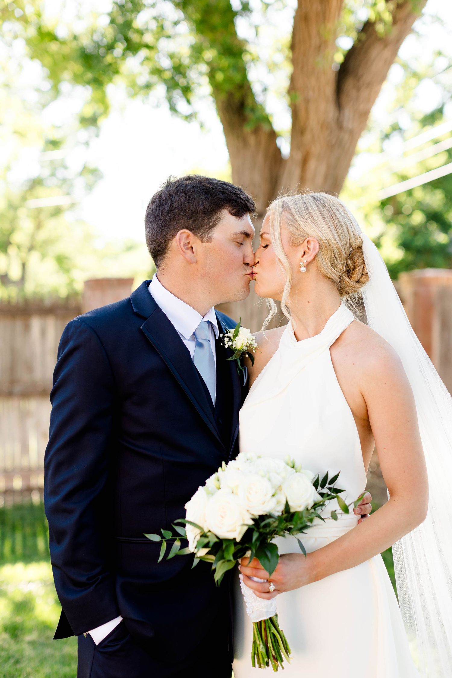 Newlyweds sharing romantic kisses in a sunlit garden setting.