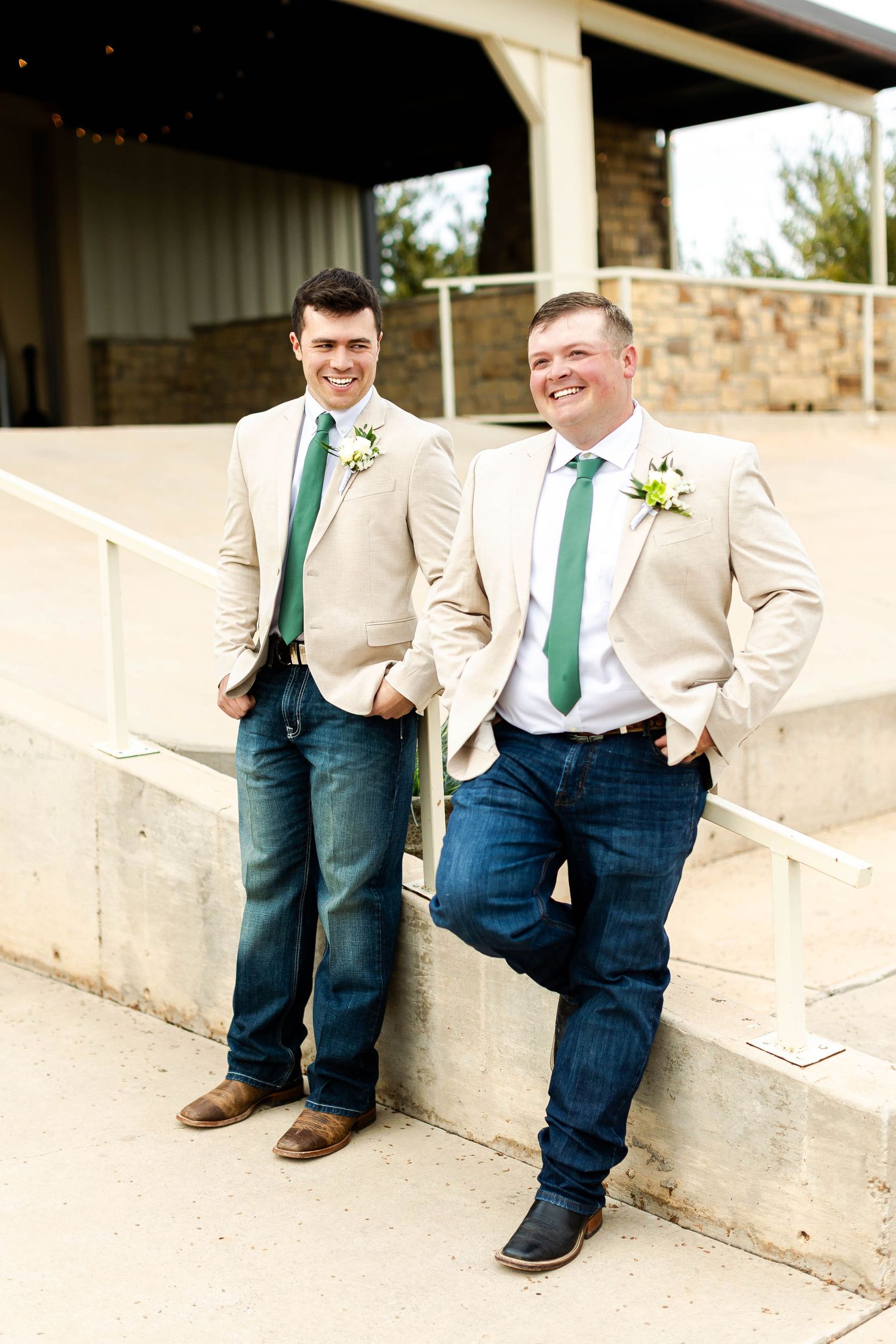Groomsmen in tan jackets and green ties pose casually on concrete steps.