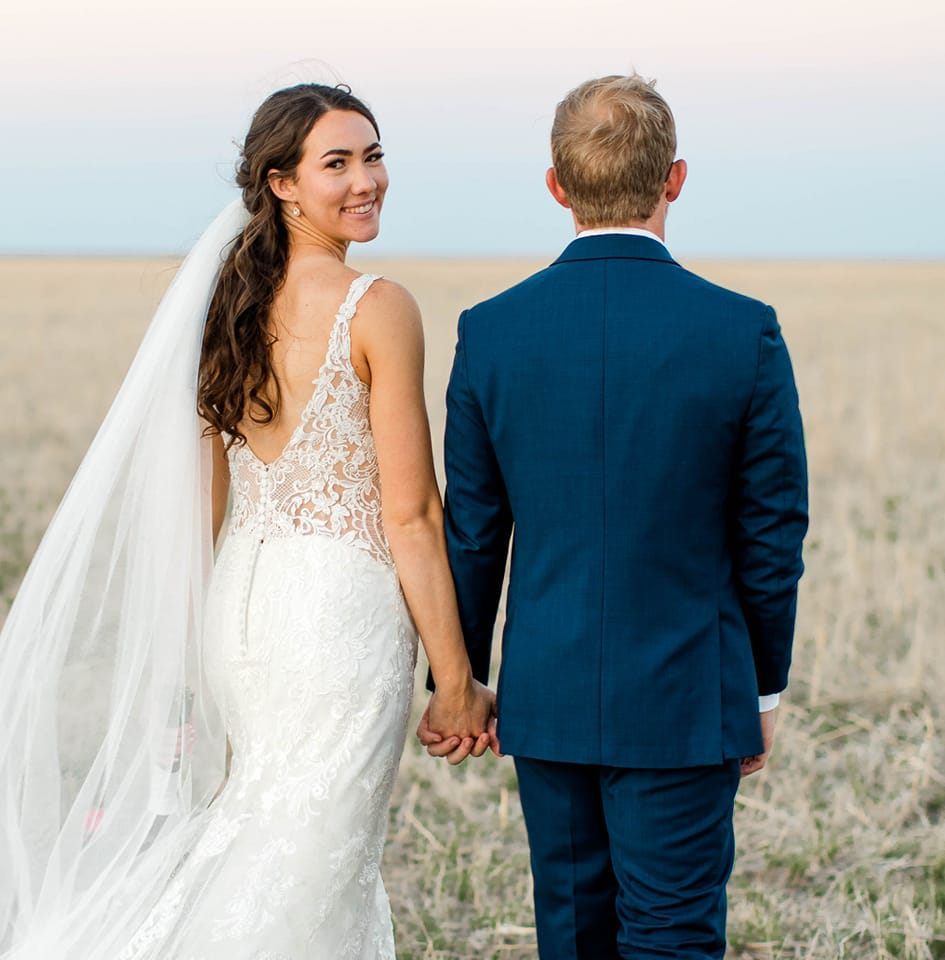 Newlywed couple walking hand in hand through a scenic field on their wedding day.