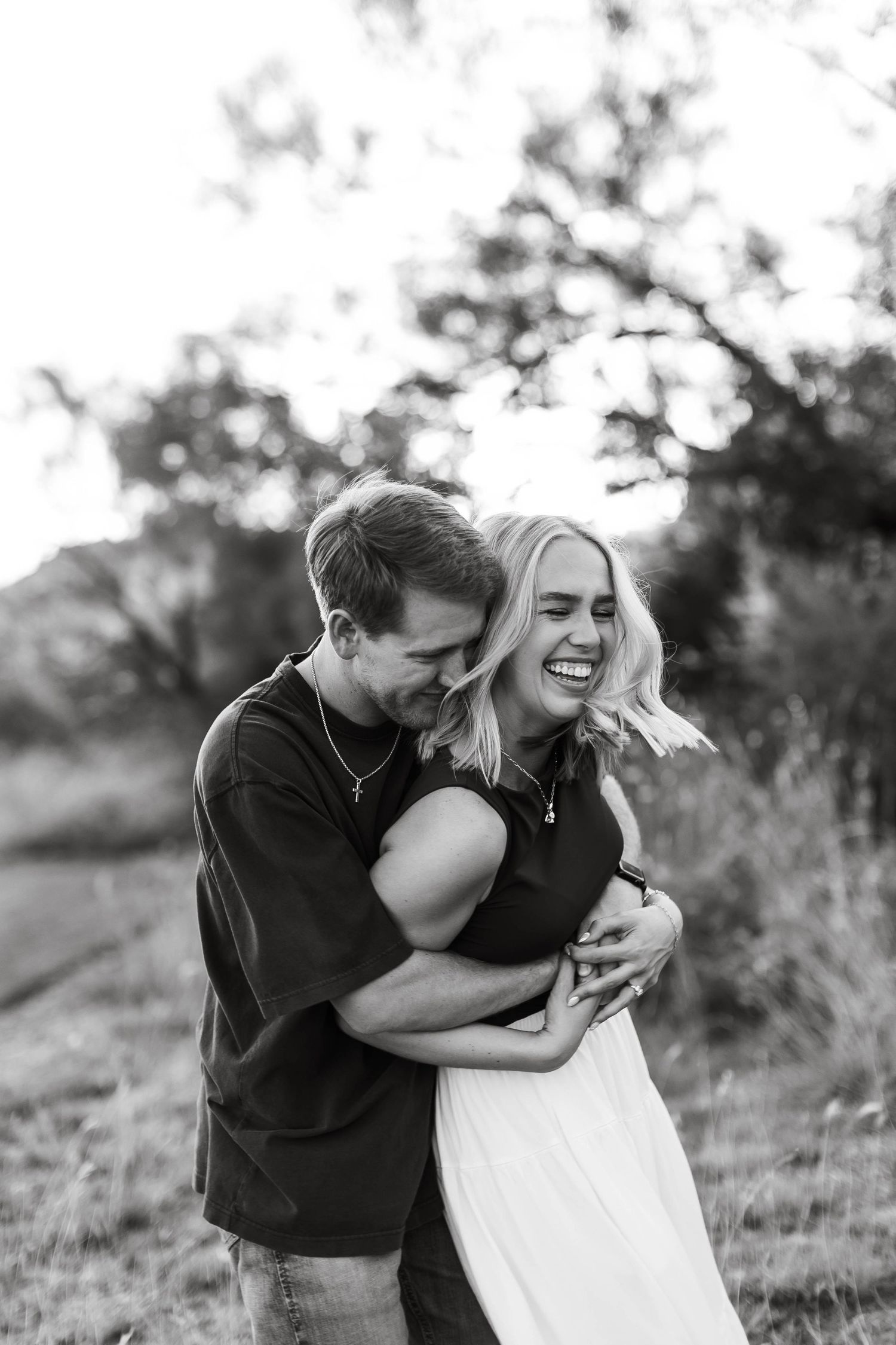 Black and white candid portrait of couple laughing together outdoors at sunset.