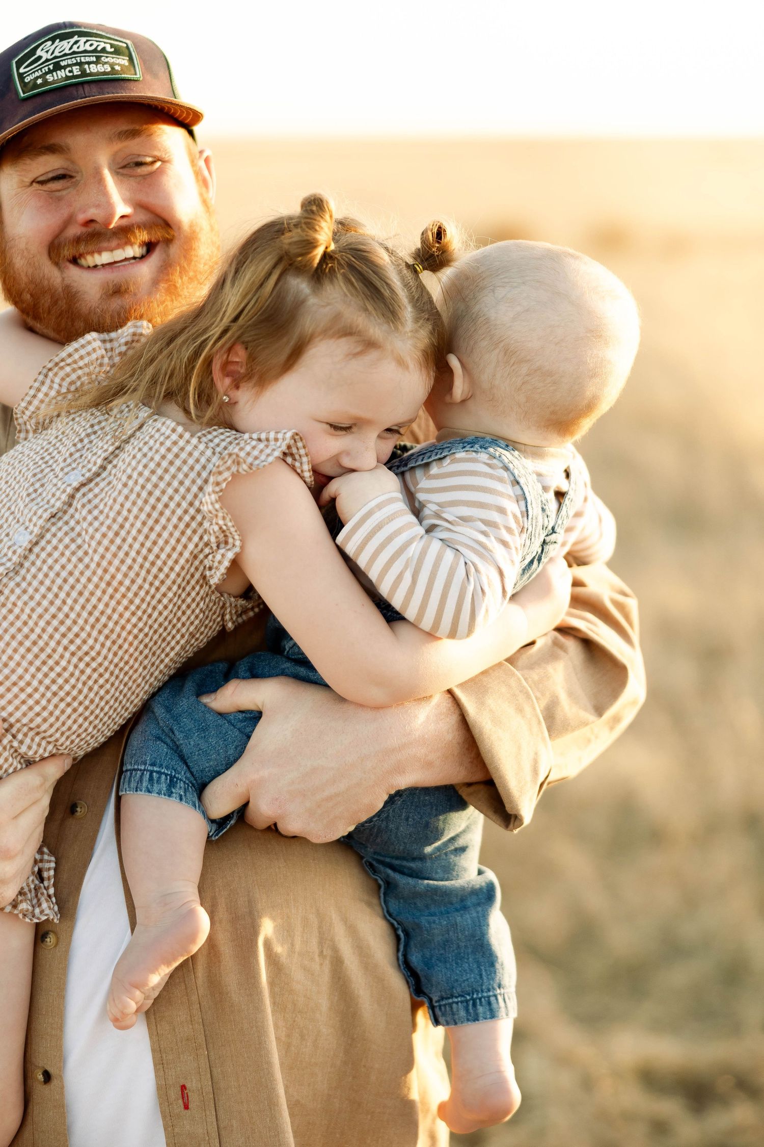 A joyful embrace between parent and children in warm sunlit field.