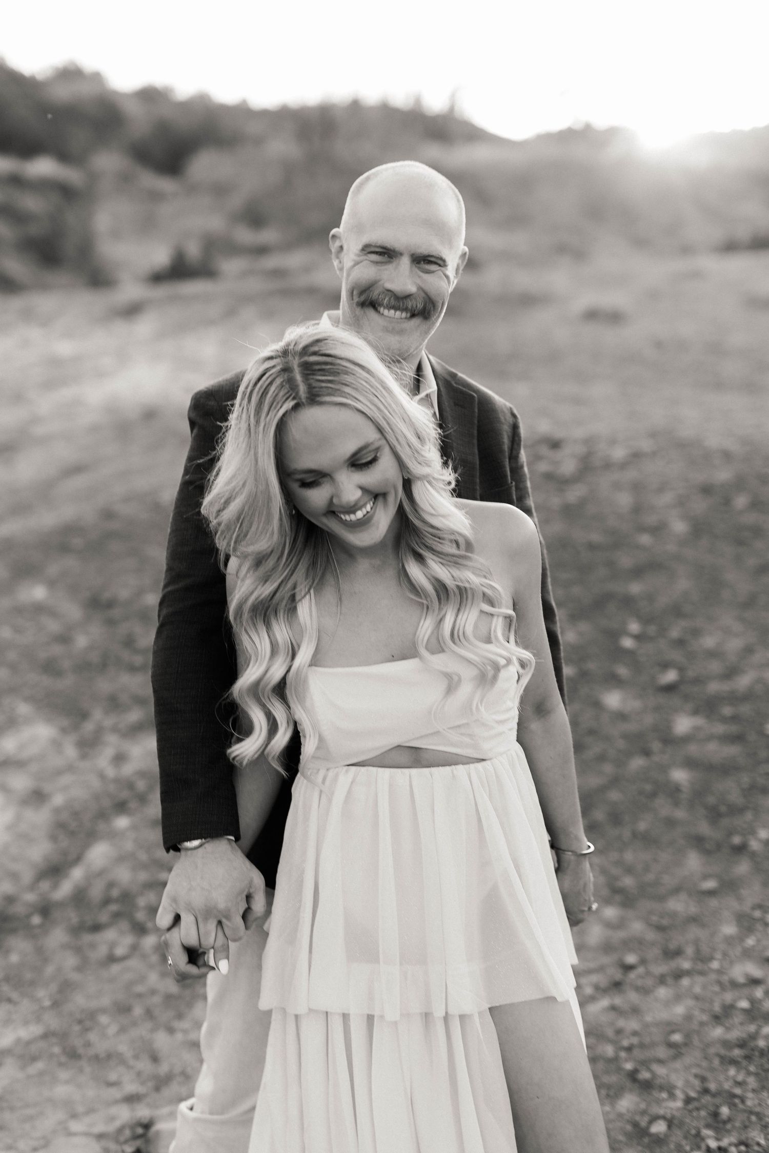 A black and white portrait of a couple sharing a joyful moment outdoors.