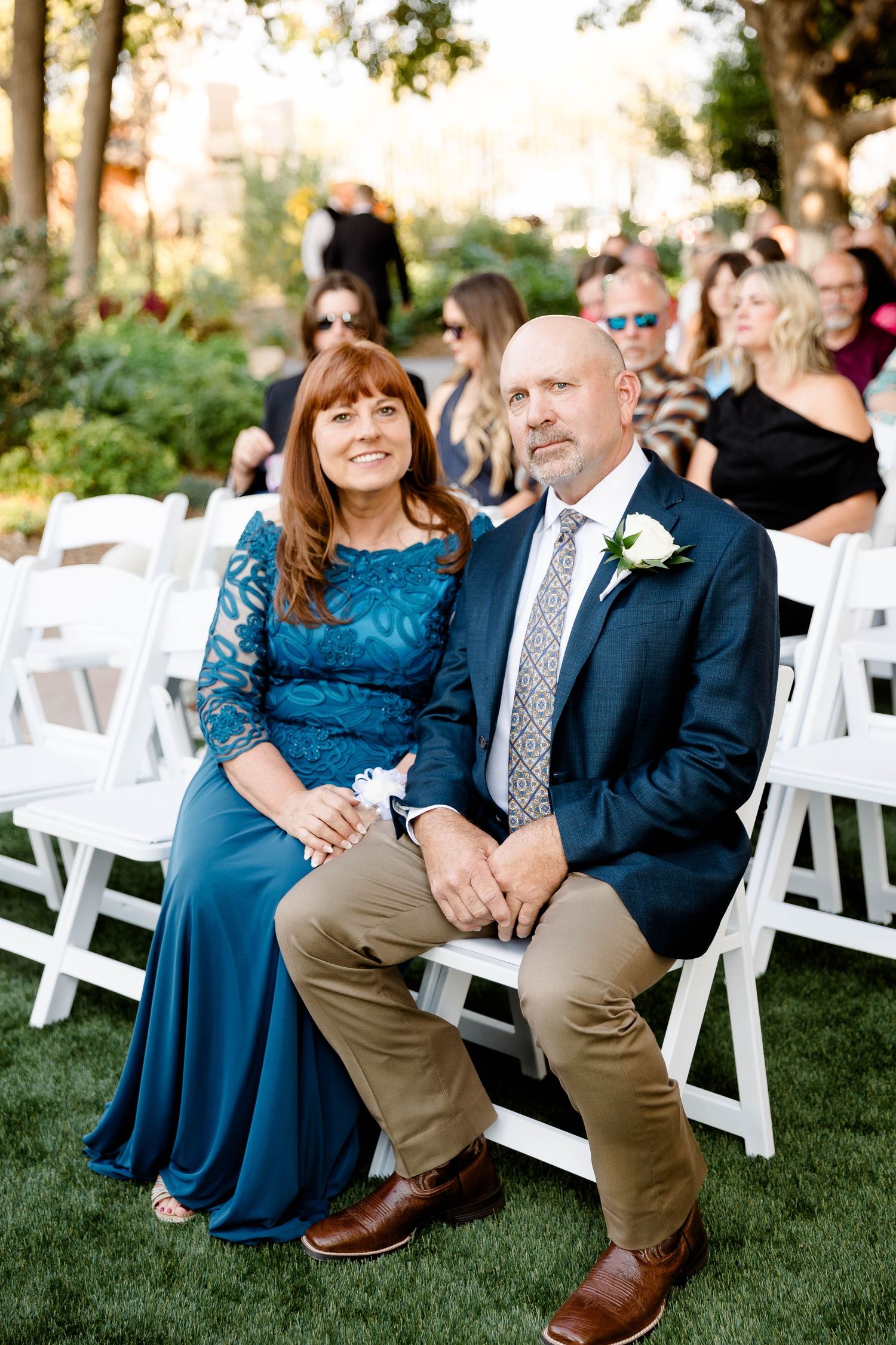 Wedding guests seated on white chairs during an outdoor ceremony.