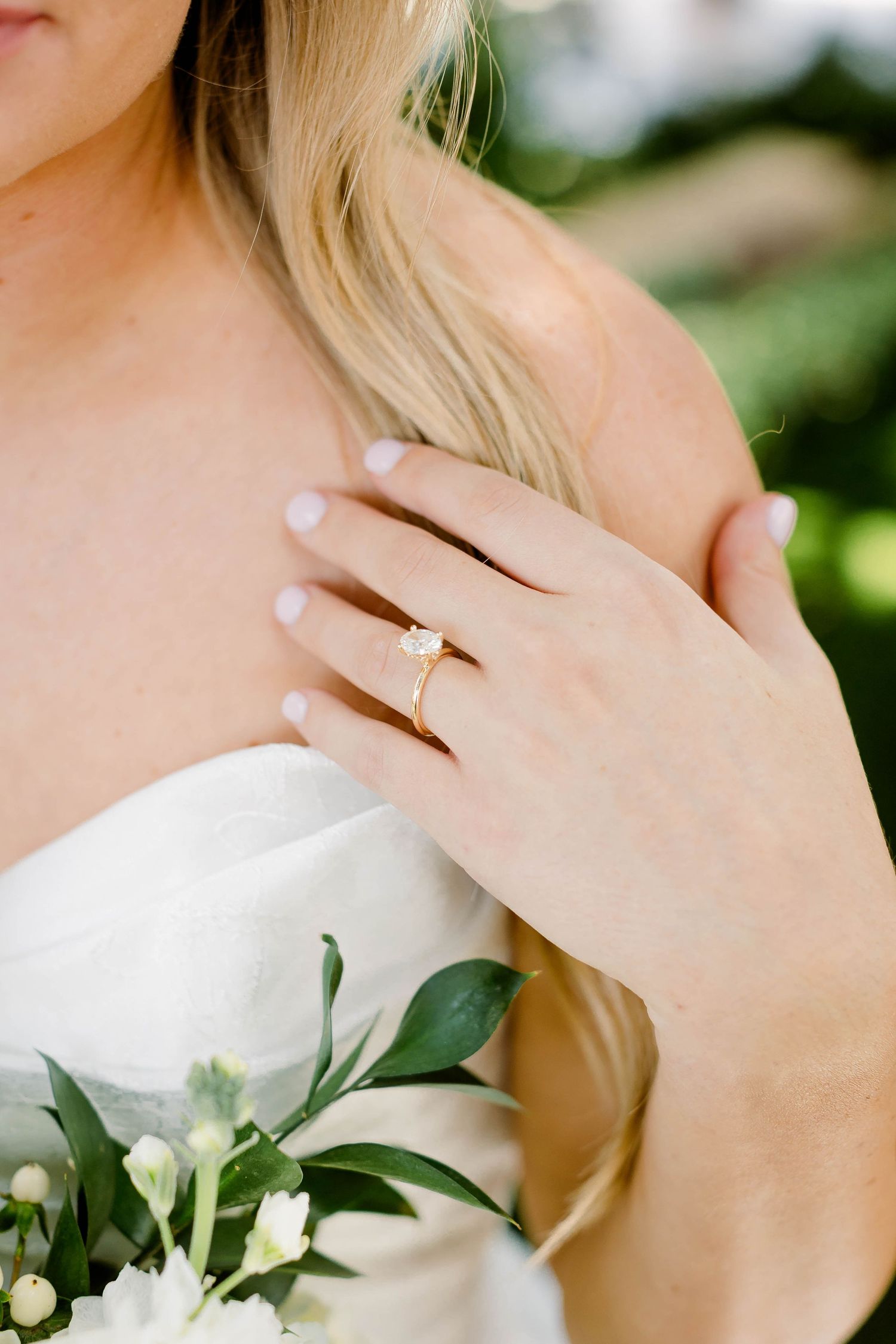 Close-up detail of hands holding white floral bouquet with engagement ring.