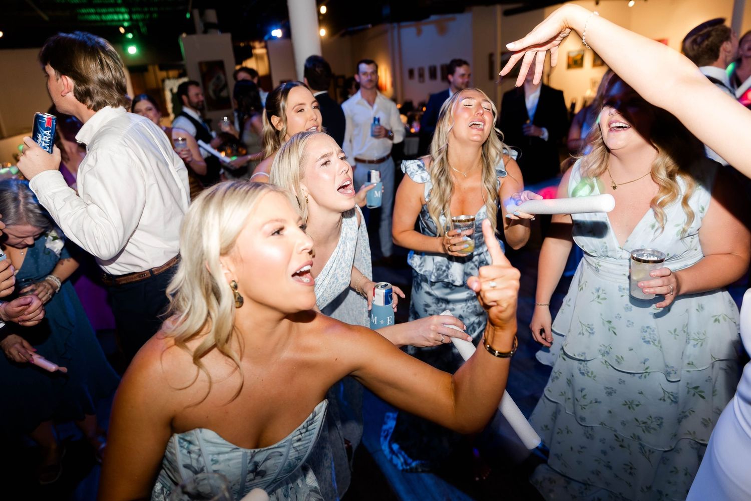 Wedding guests dancing and celebrating with drinks on the dance floor.