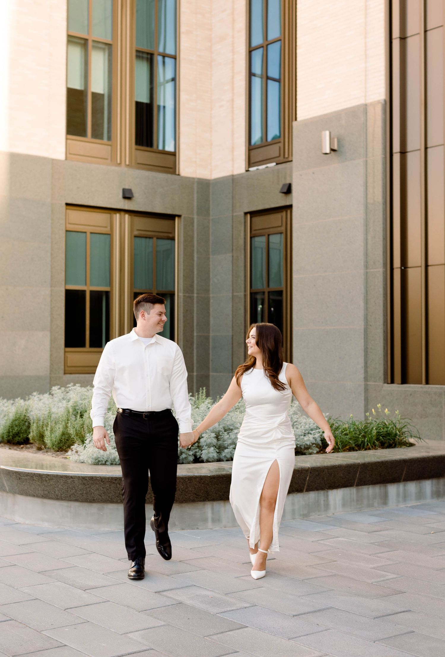 Couple in formal attire walking hand in hand outside contemporary building.
