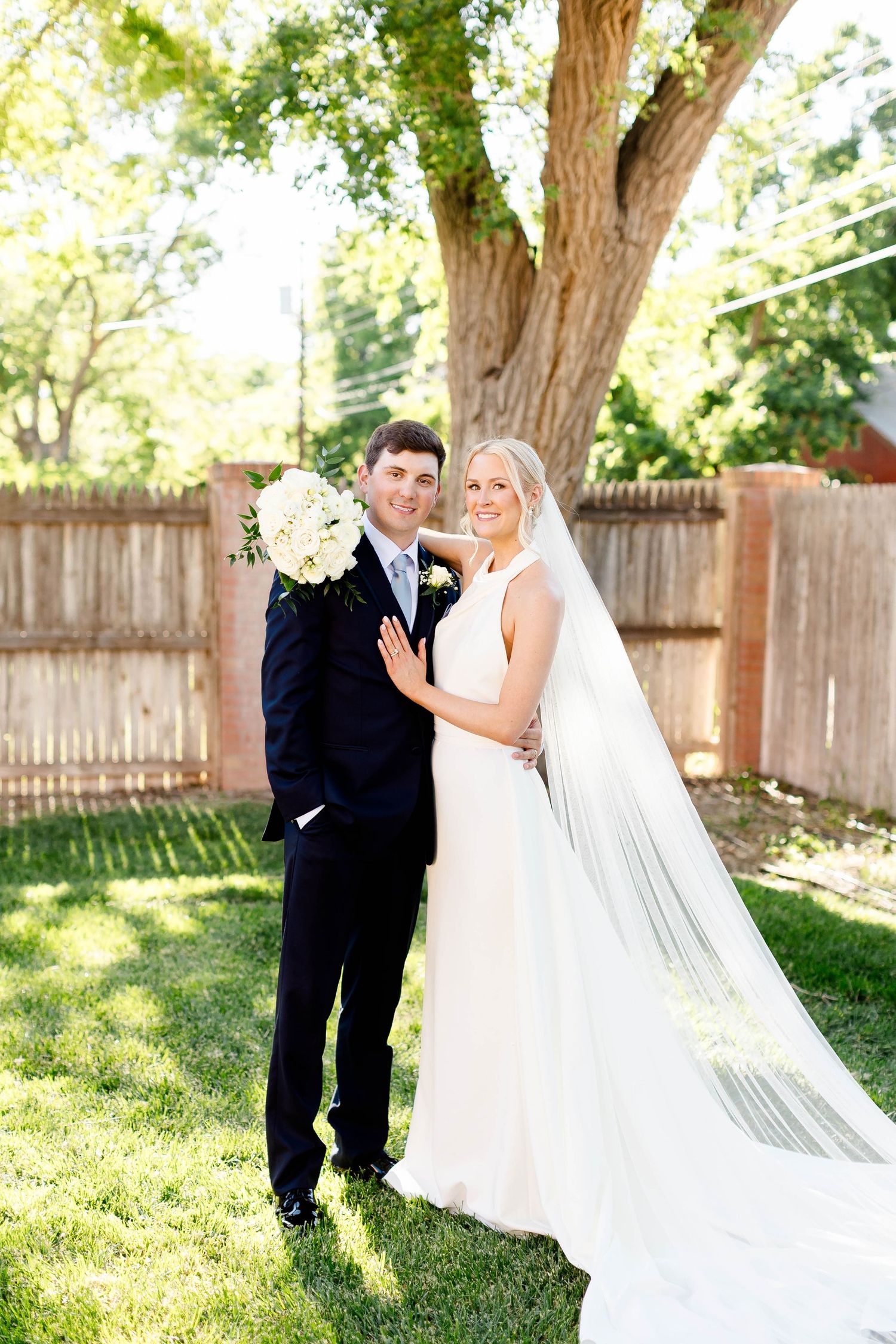 Newlyweds sharing playful moments in a sunlit garden with white flowers.
