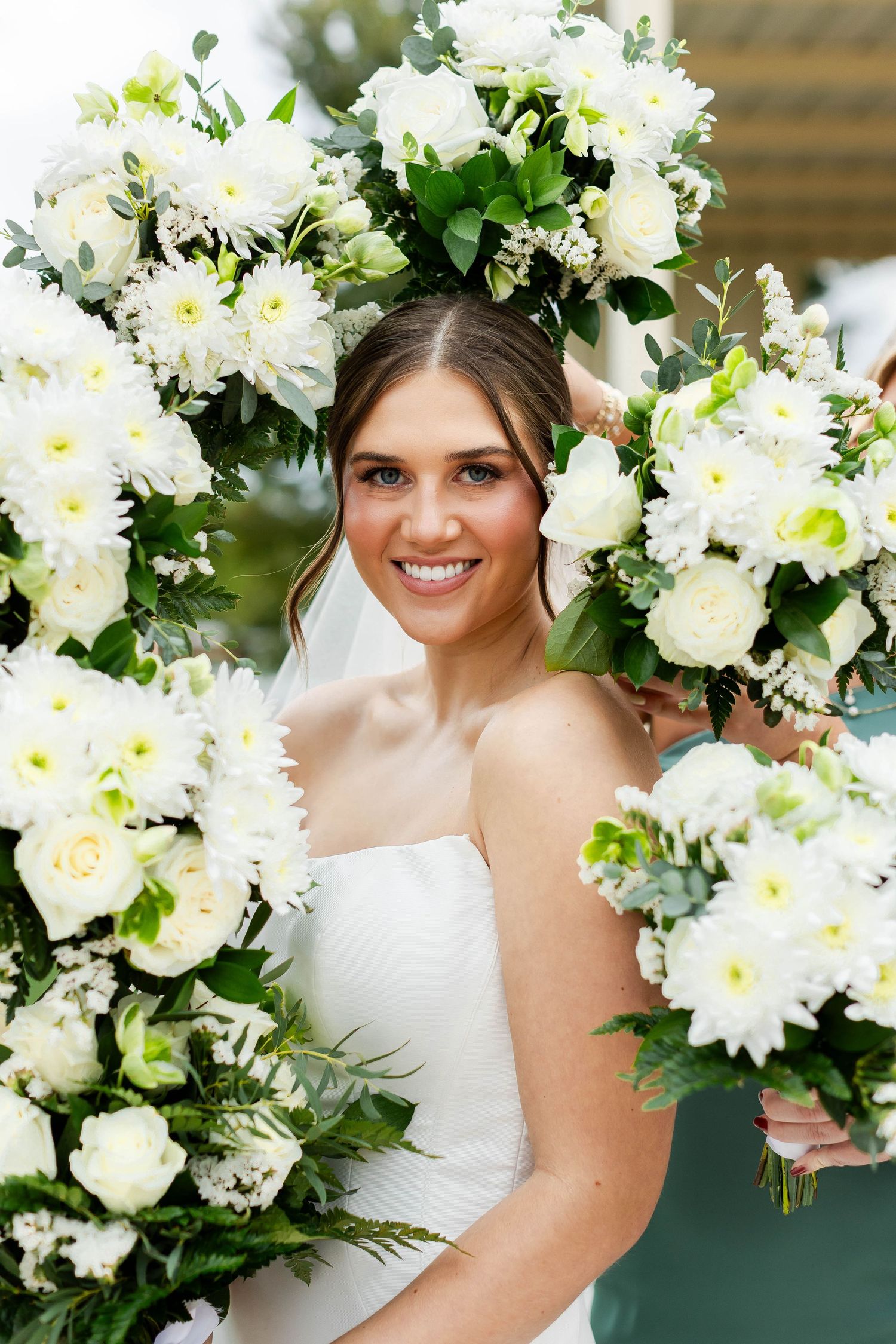 A stunning white bridal bouquet featuring roses, chrysanthemums and greenery in a classic wedding arrangement.