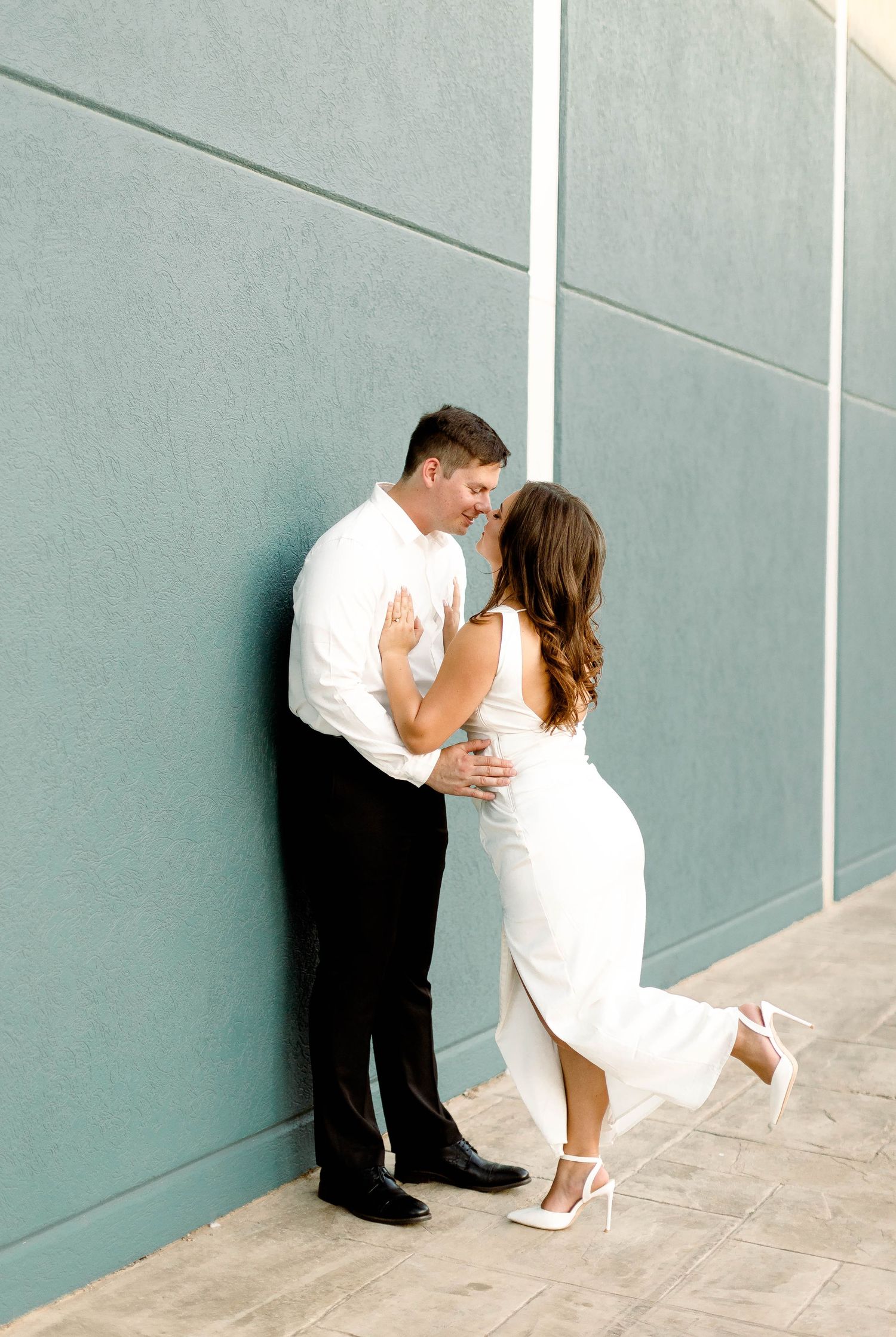 A couple shares a romantic moment against a modern teal wall and tiled floor.