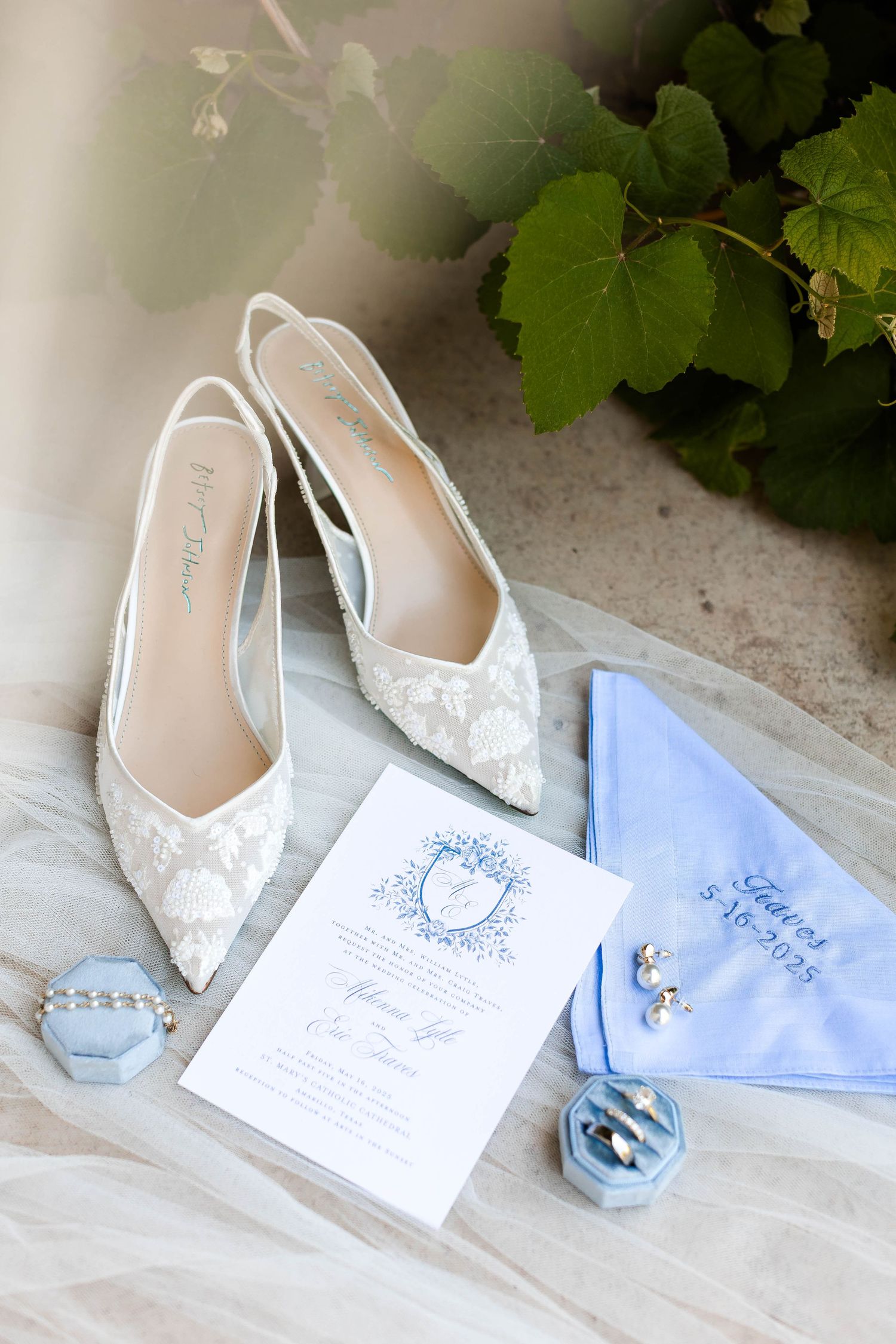 Elegant white bridal shoes displayed with light blue wedding invitations and delicate accessories.