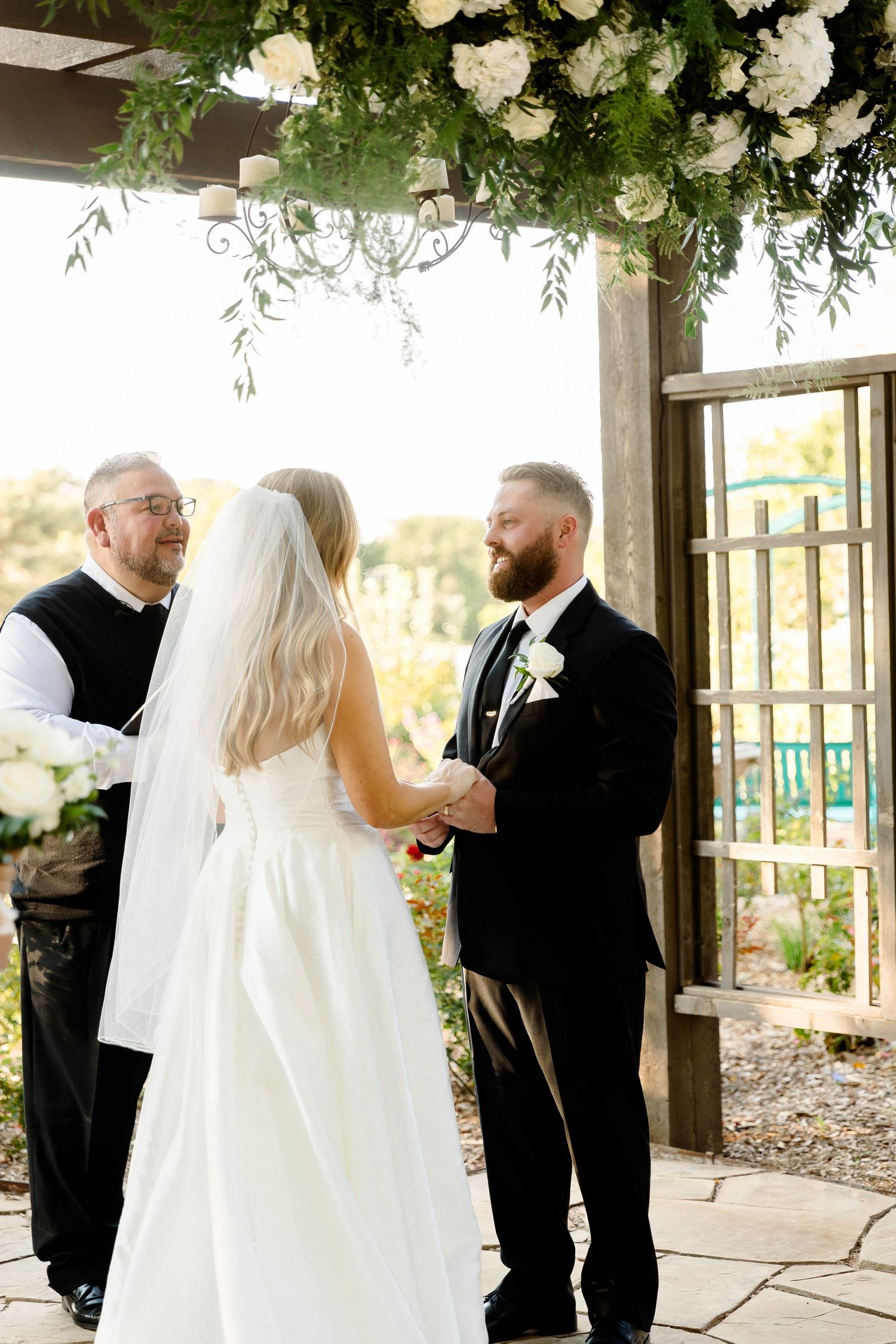 Wedding first look moment under a covered pavilion decorated with white flowers and greenery.