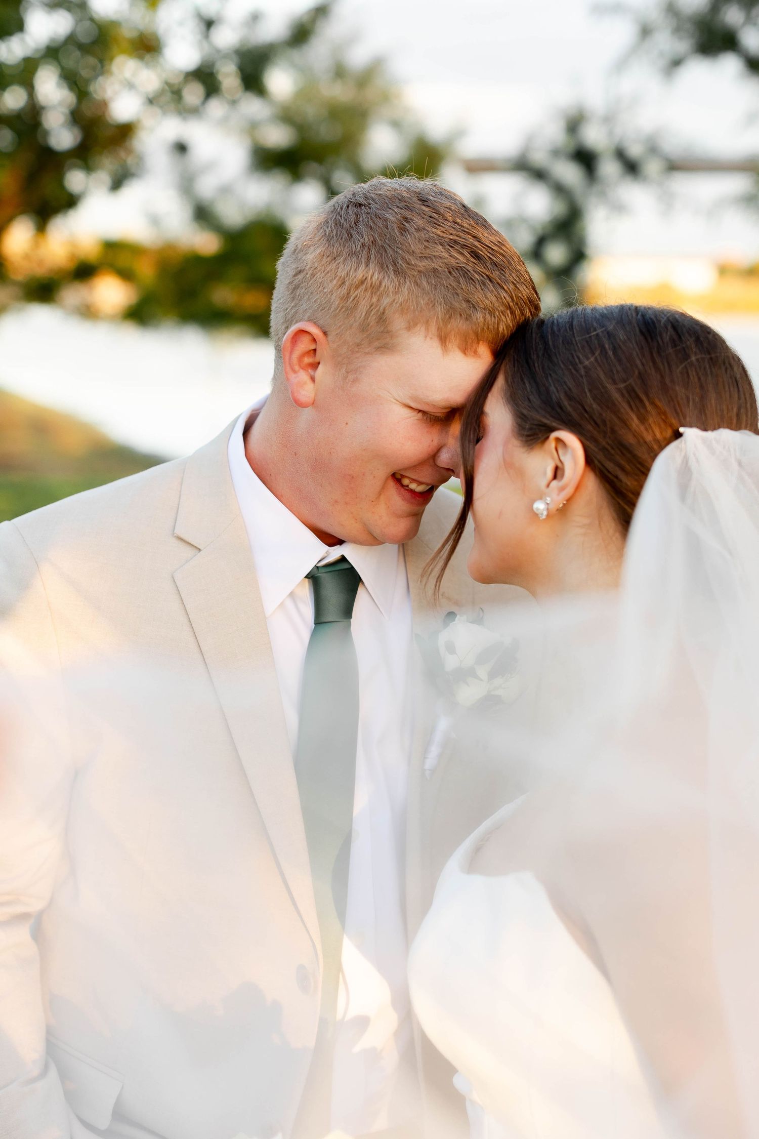 Romantic wedding couple shares intimate moments in soft golden light wearing white and beige attire.