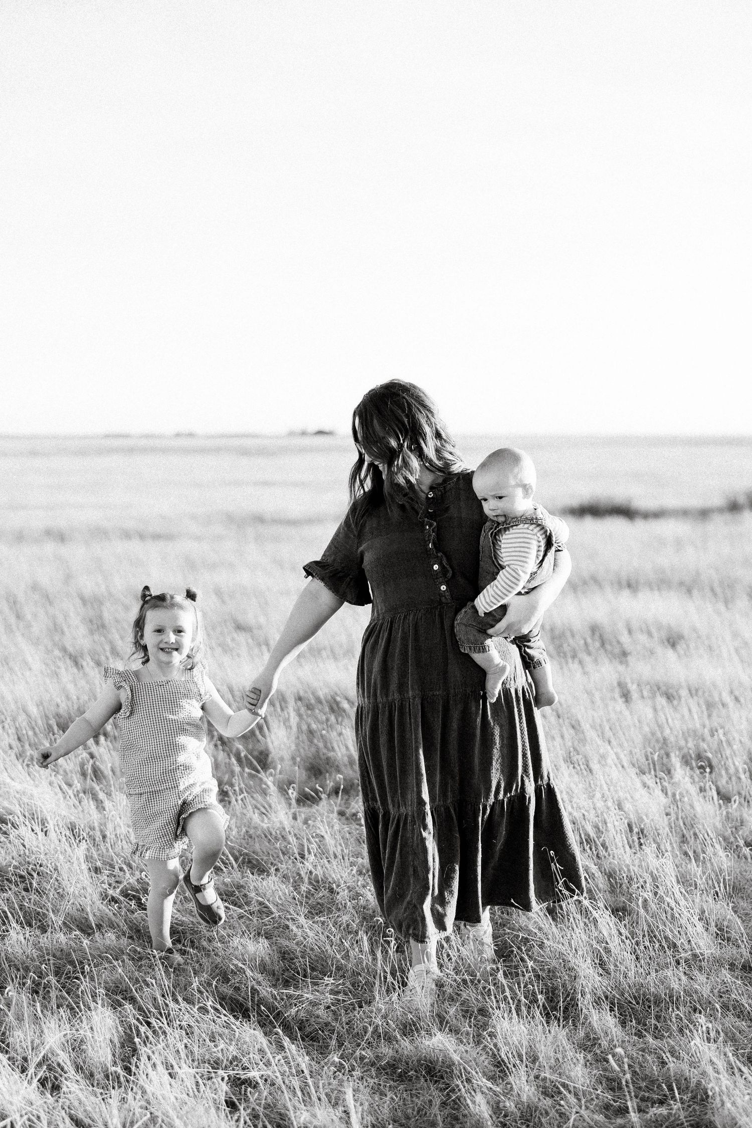 A joyful sequence of black and white photos showing a toddler running through tall grass towards adults in a field.