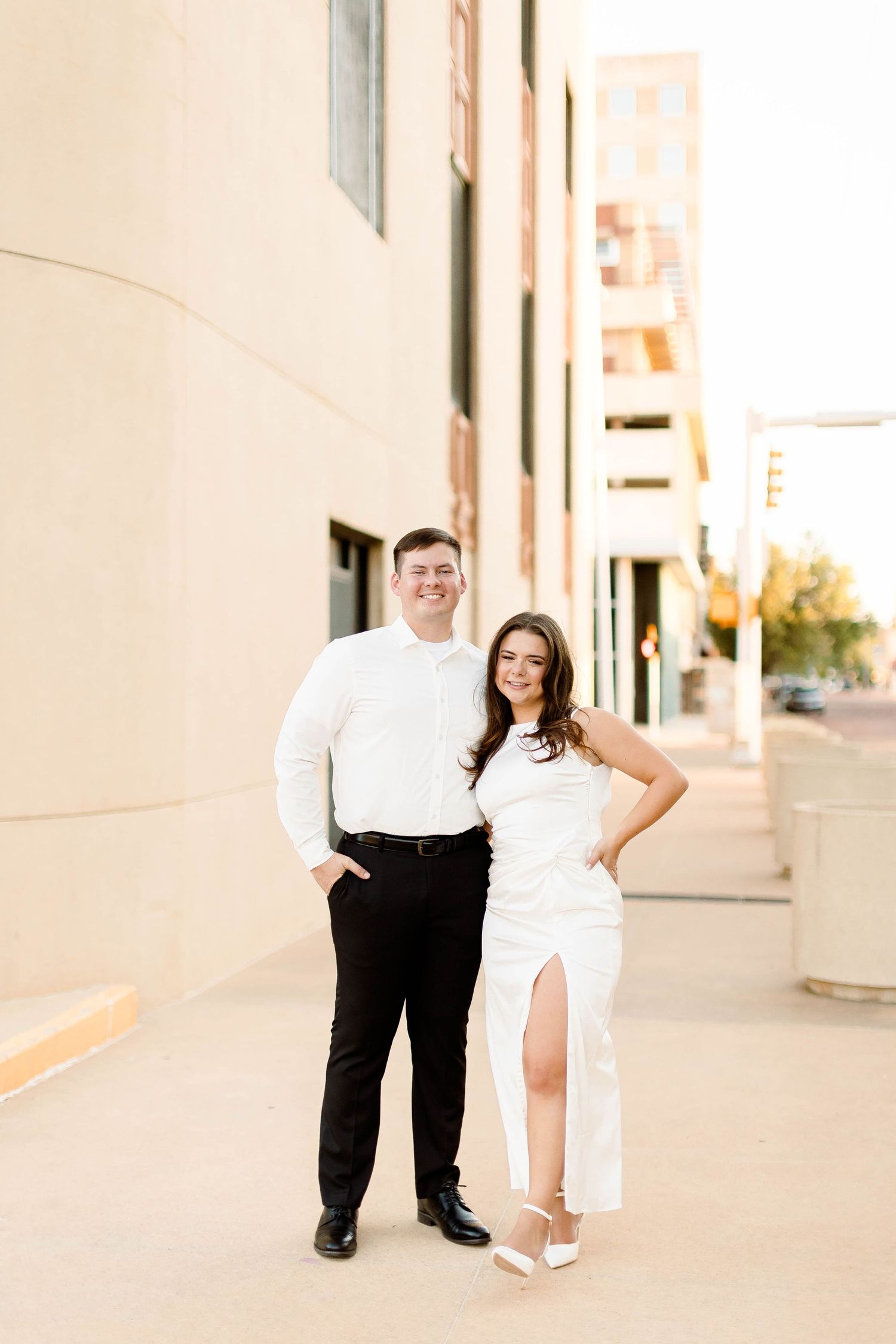 A couple poses playfully against a modern building exterior in contrasting outfits.
