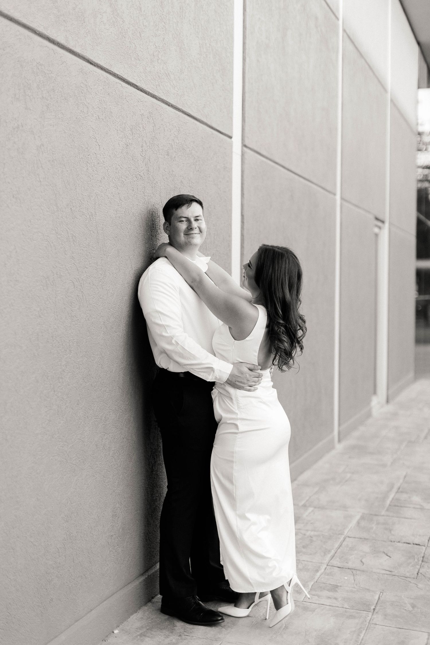 A romantic black and white engagement photo series showing a couple embracing against a light colored wall.