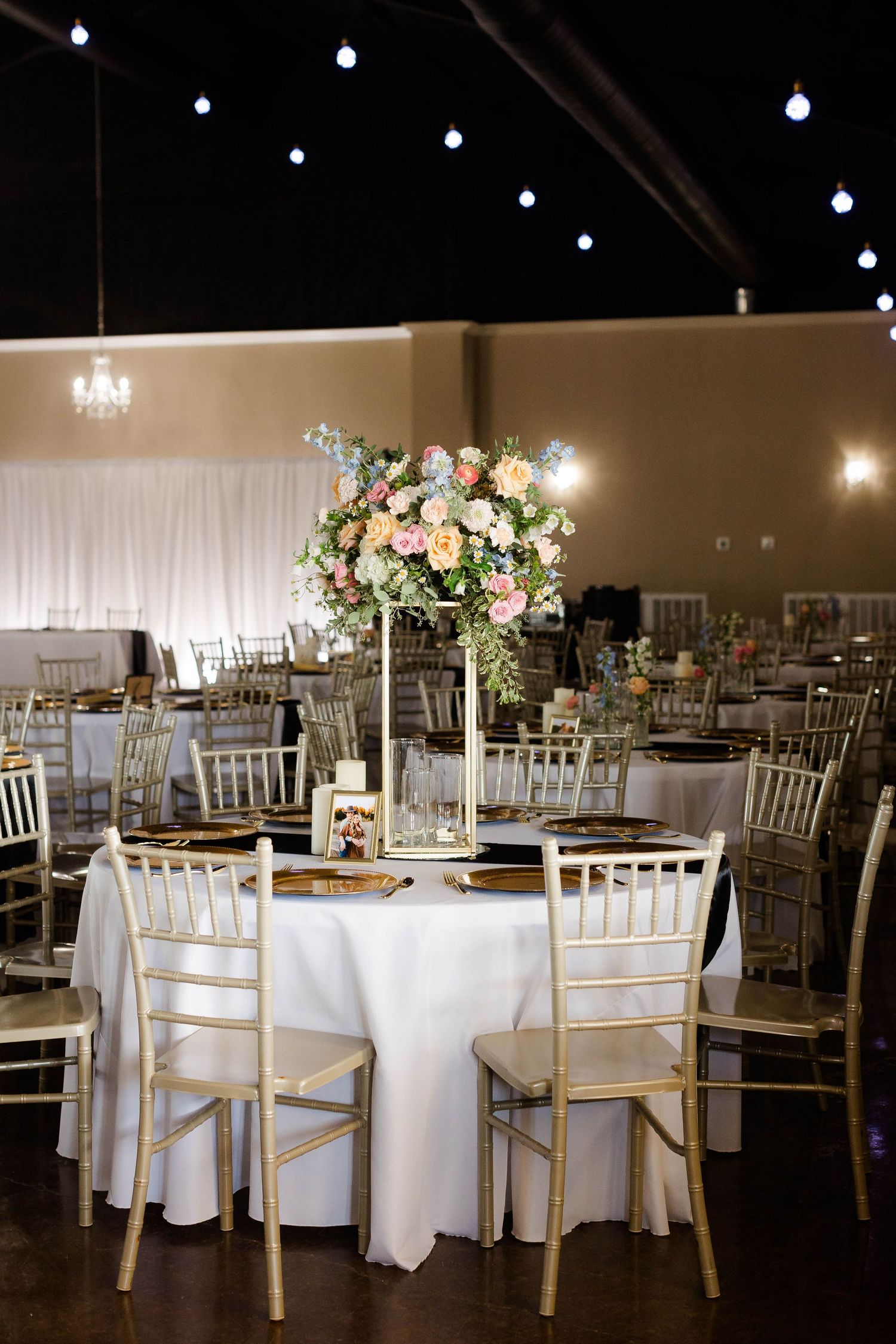 Elegant wedding reception setup with white linens and gold chiavari chairs under string lights.