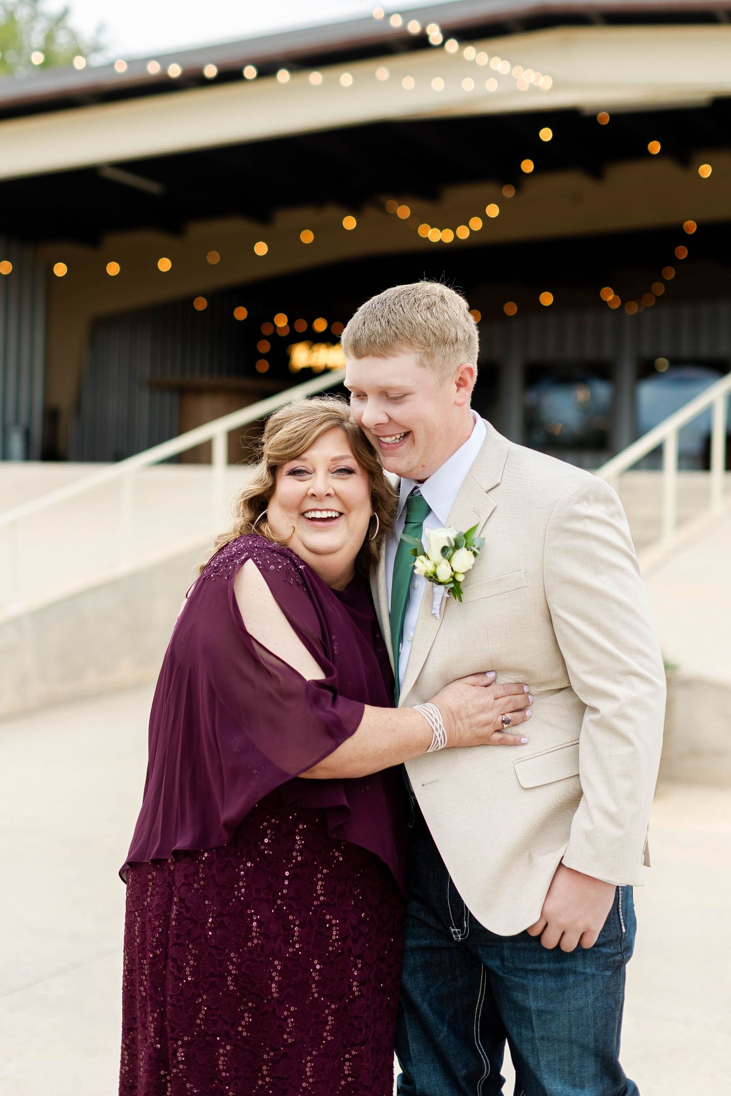 Wedding party members share joyful moments under string lights with purple and cream attire.