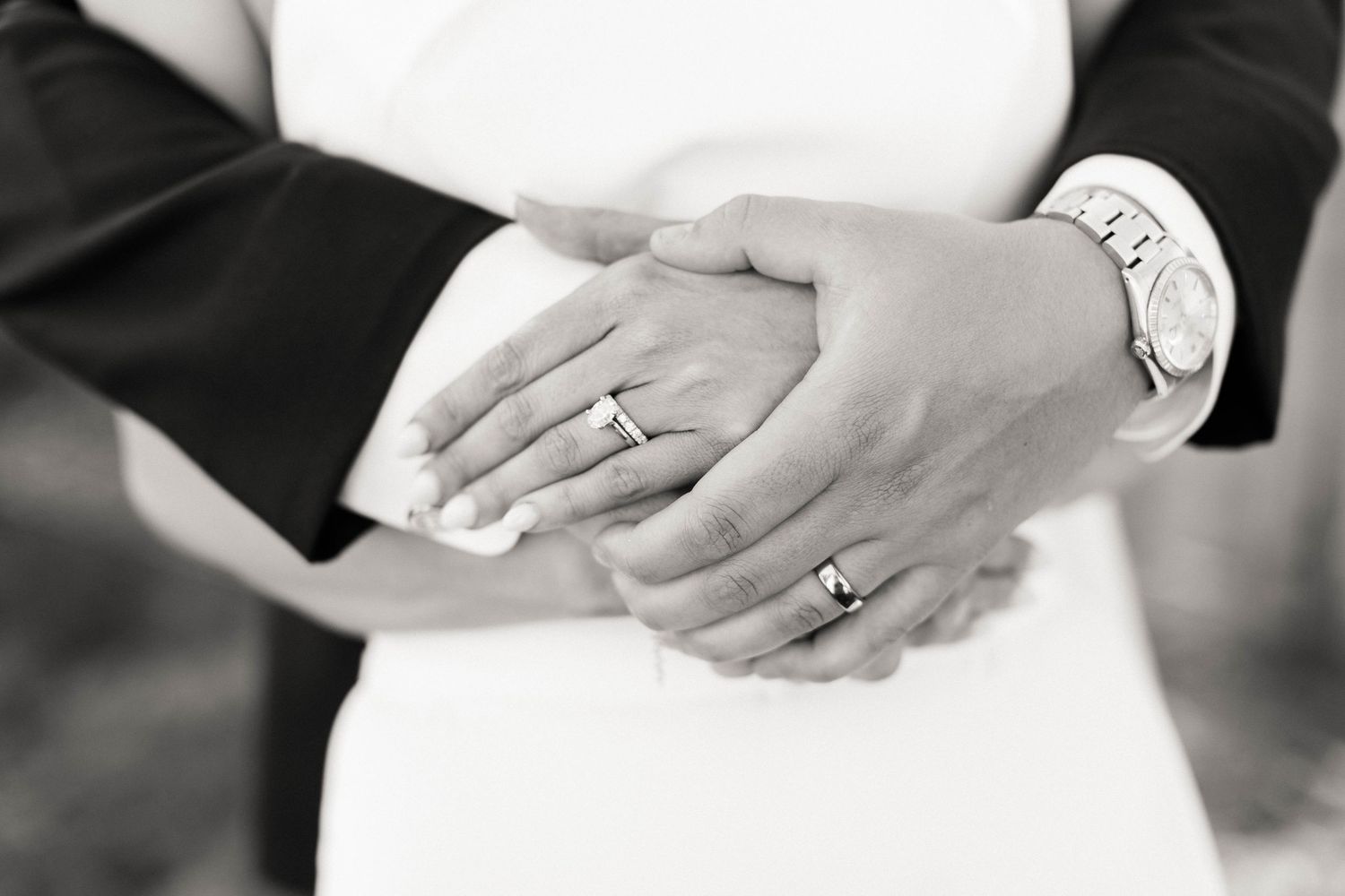 Black and white close-up of wedding rings and hands against a white dress.