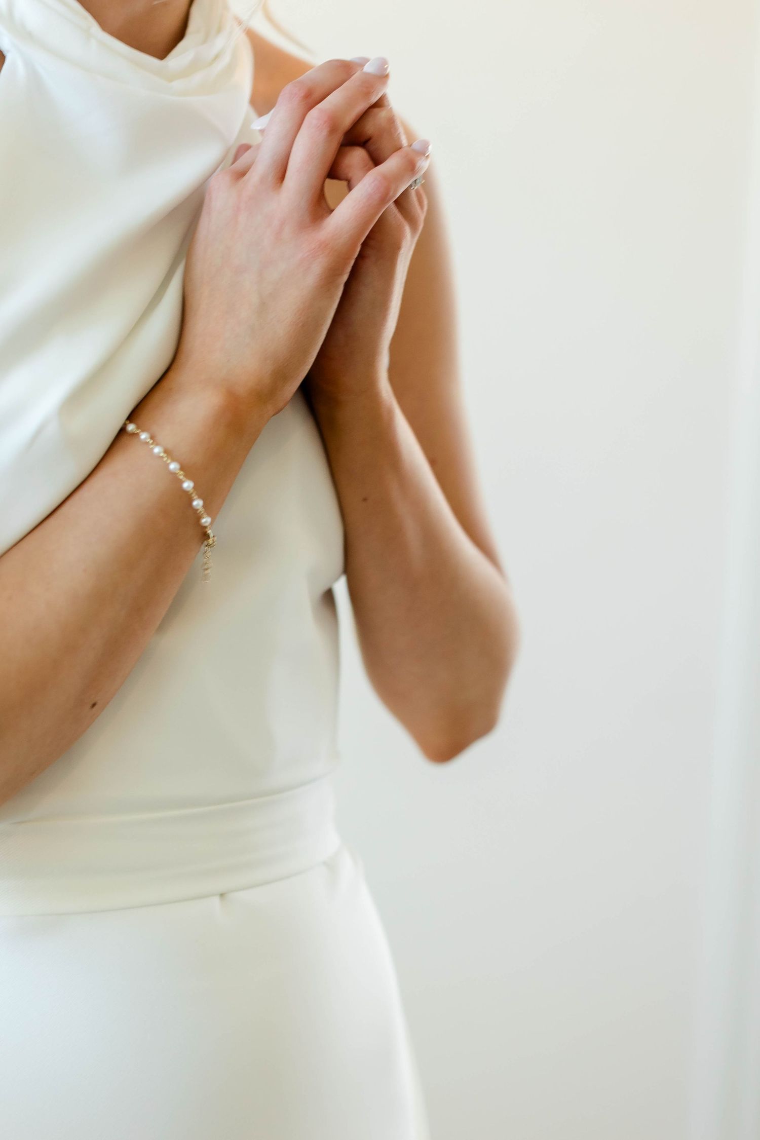 Close-up details of hands and pearls against a classic white wedding dress.