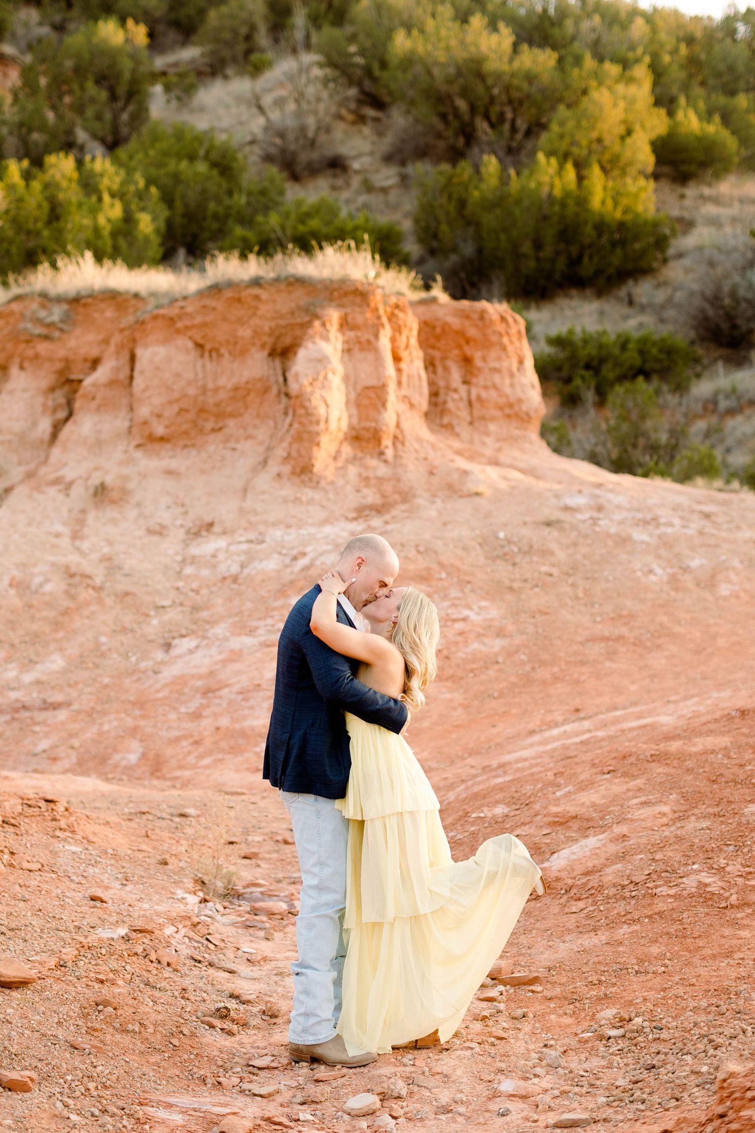 Romantic moment captured between couple on red rock formations in desert setting.