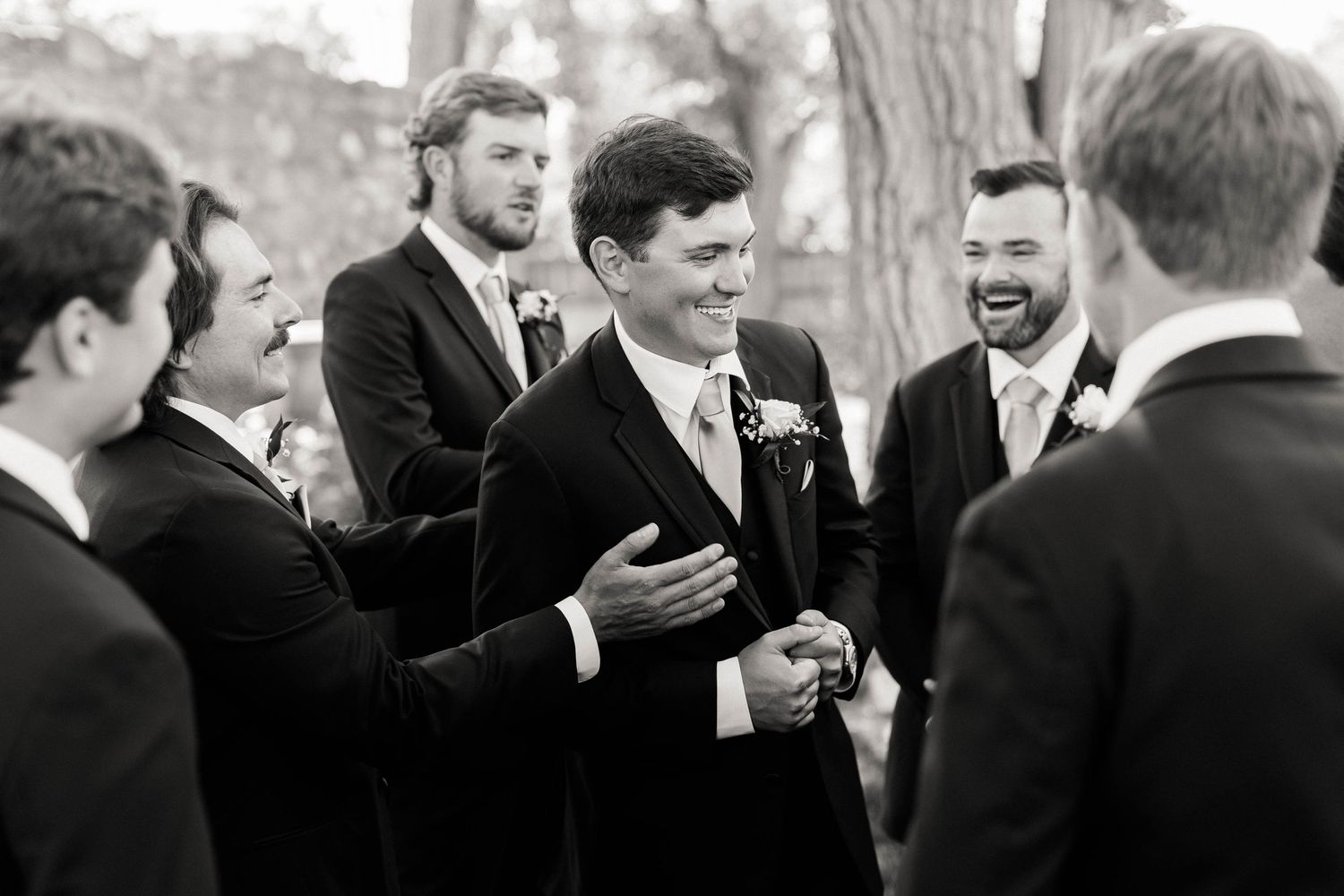 A group of groomsmen share a candid moment and laugh together during wedding photos.