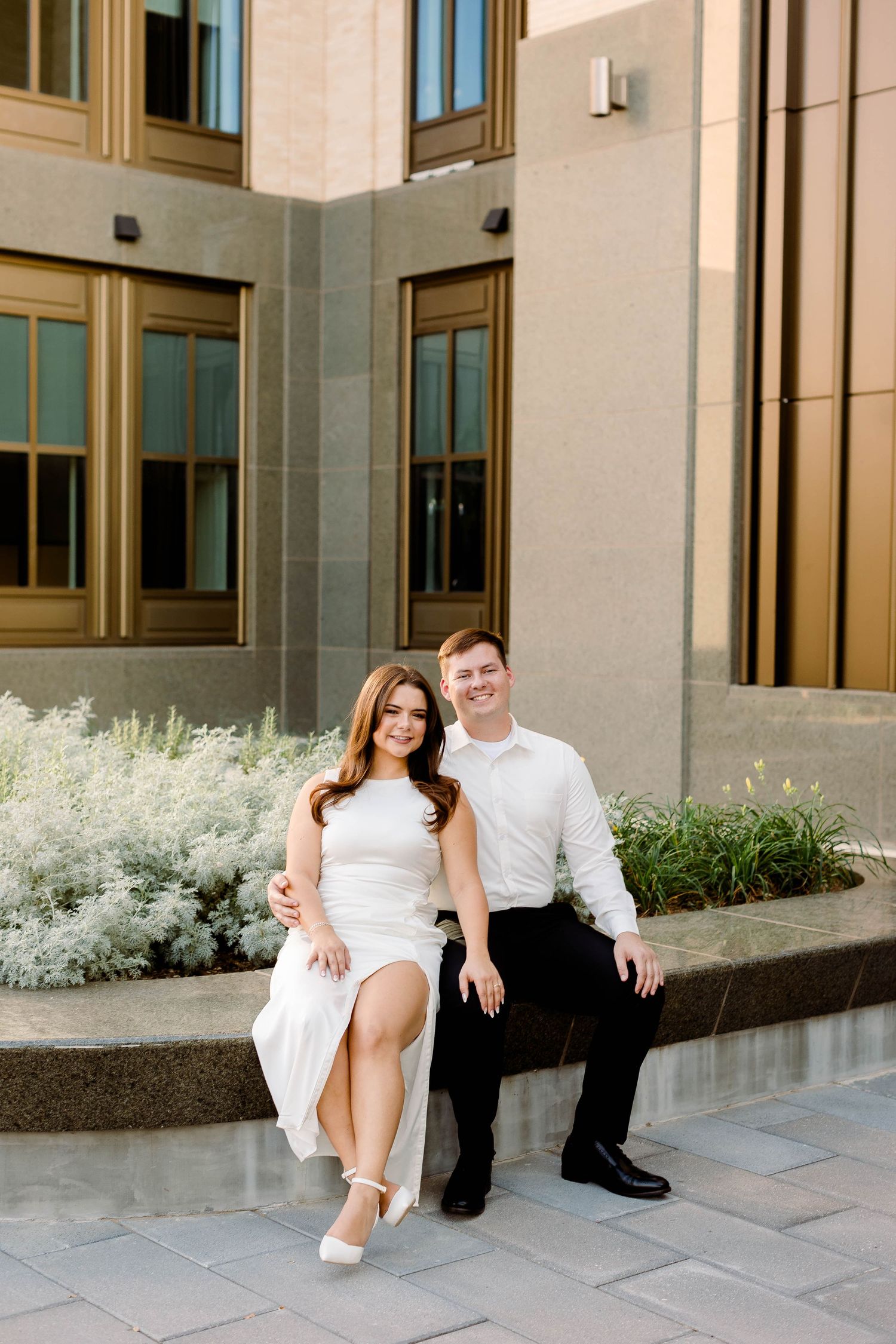 Couple in white and black outfits poses casually on modern building steps.